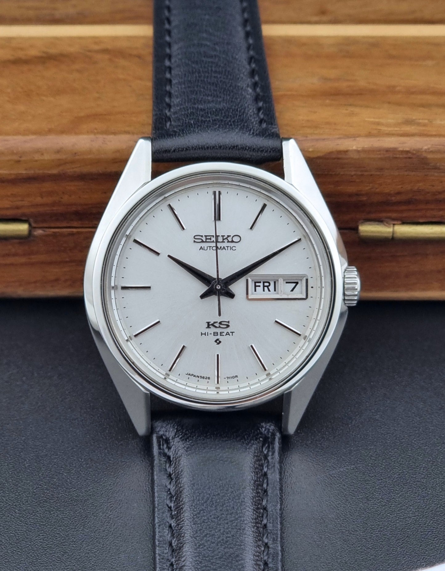 Vintage King Seiko Wristwatch with black leather strap and silver case on a wooden surface front