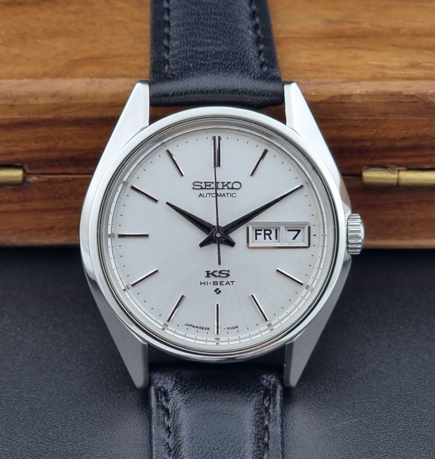 Vintage King Seiko Wristwatch with black leather strap and silver case on a wooden surface dial view