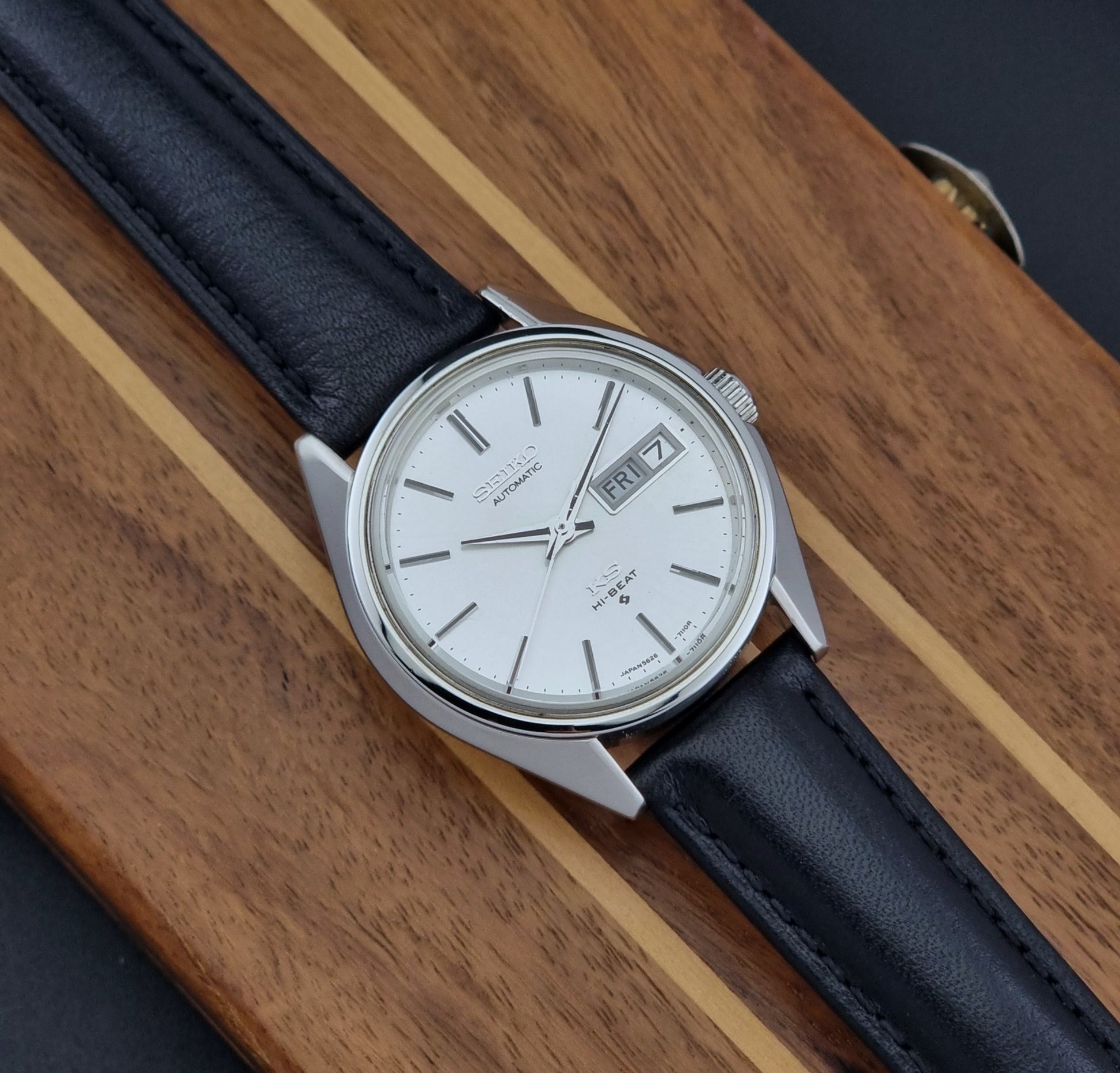 Vintage King Seiko Wristwatch with black leather strap and silver case on a wooden surface front view