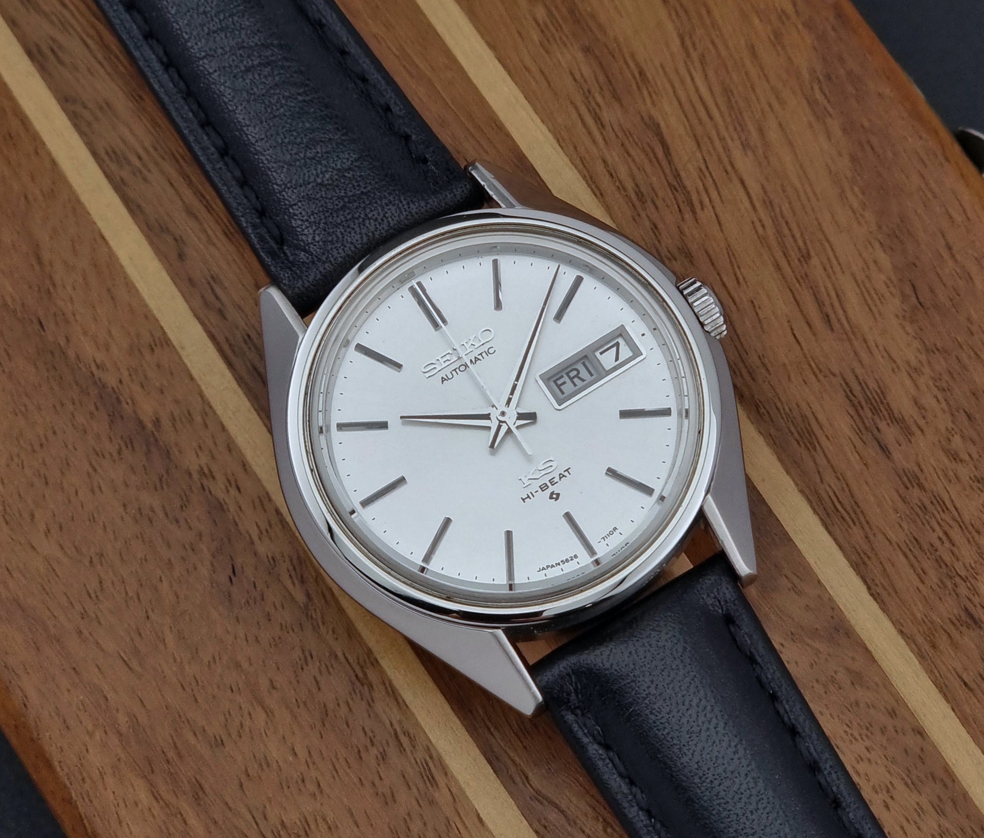 Vintage King Seiko Wristwatch with black leather strap and silver case on a wooden surface close view