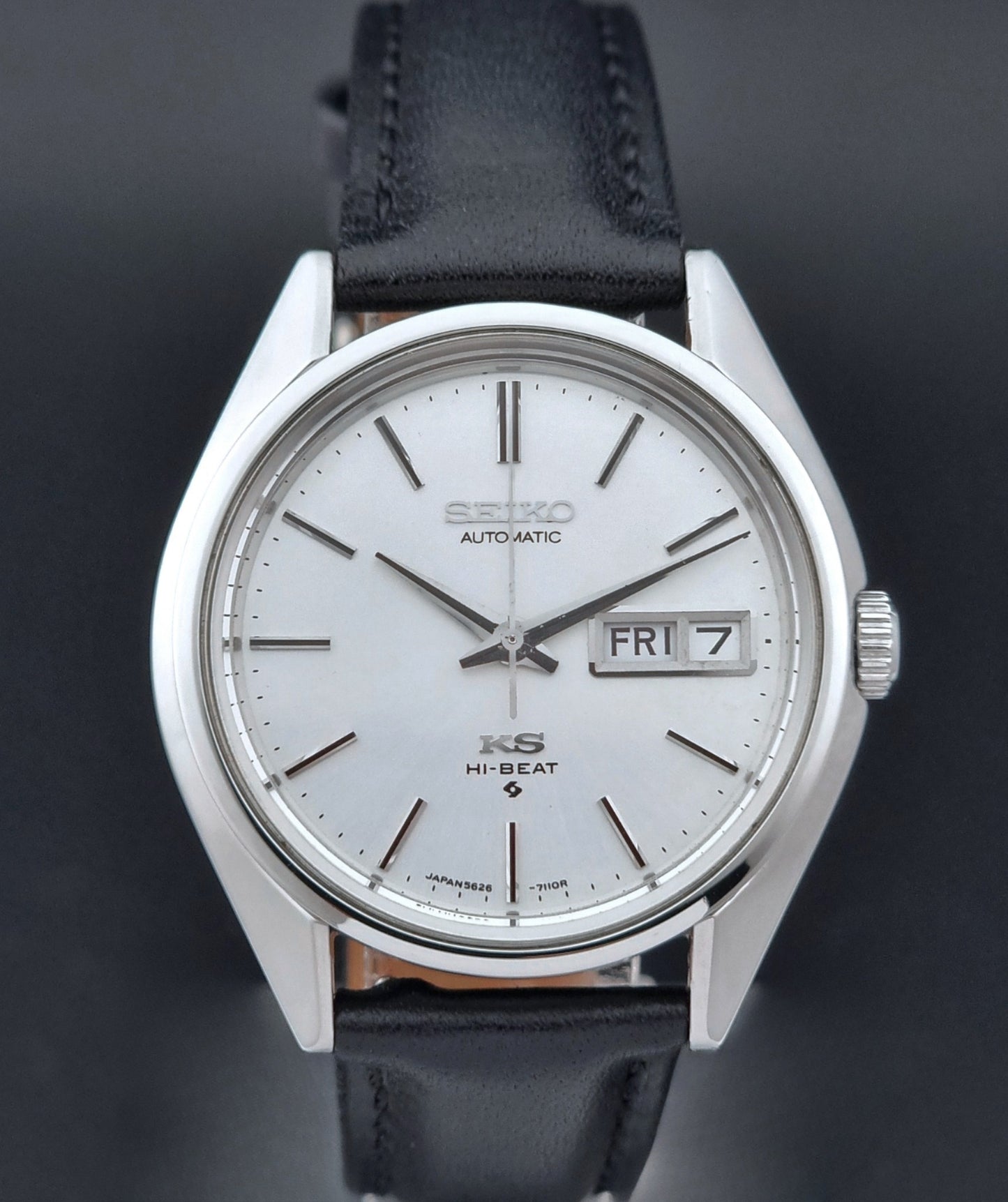 Vintage King Seiko Wristwatch with black leather strap and silver case on a wooden surface close up view