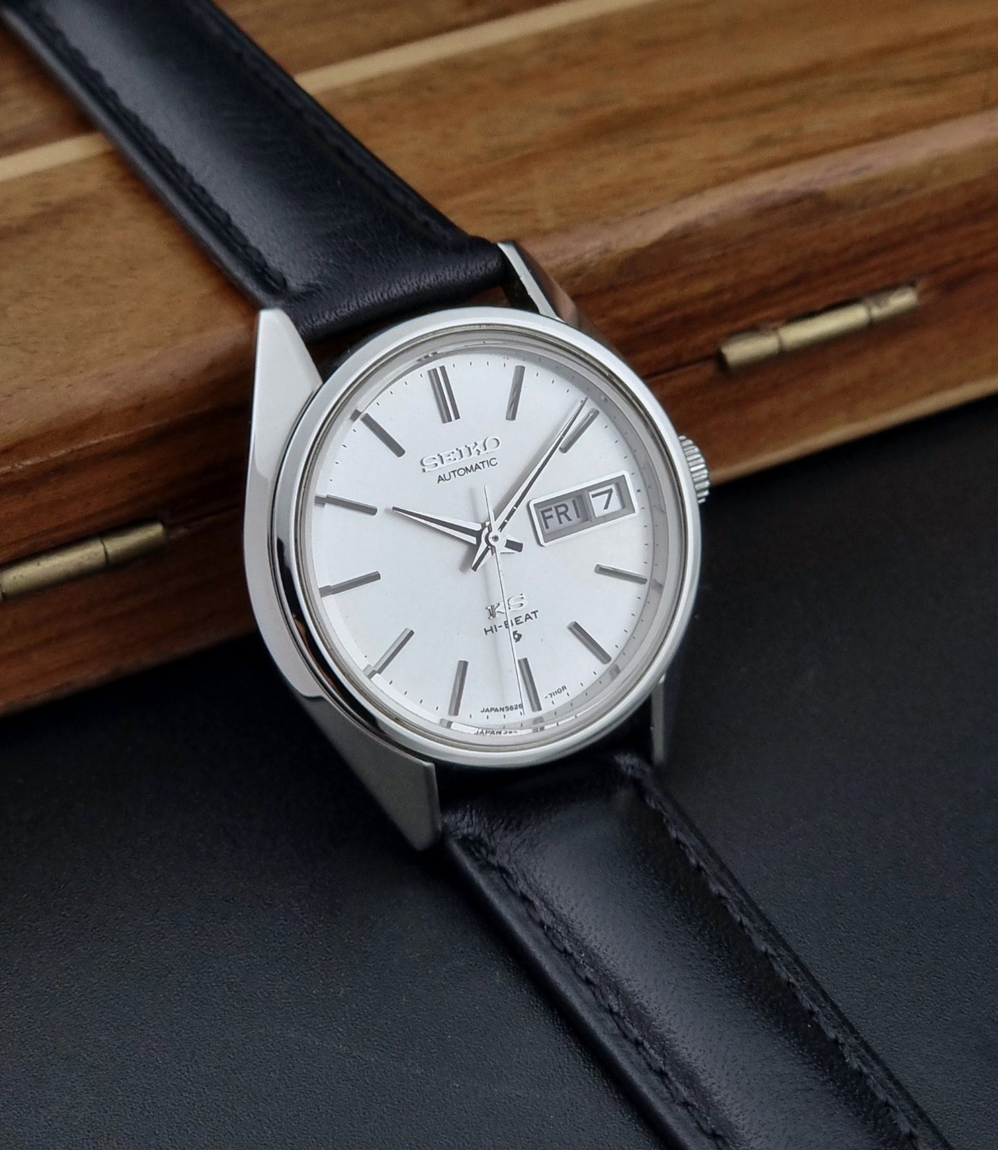 Vintage King Seiko Wristwatch with black leather strap and silver case on a wooden surface side view