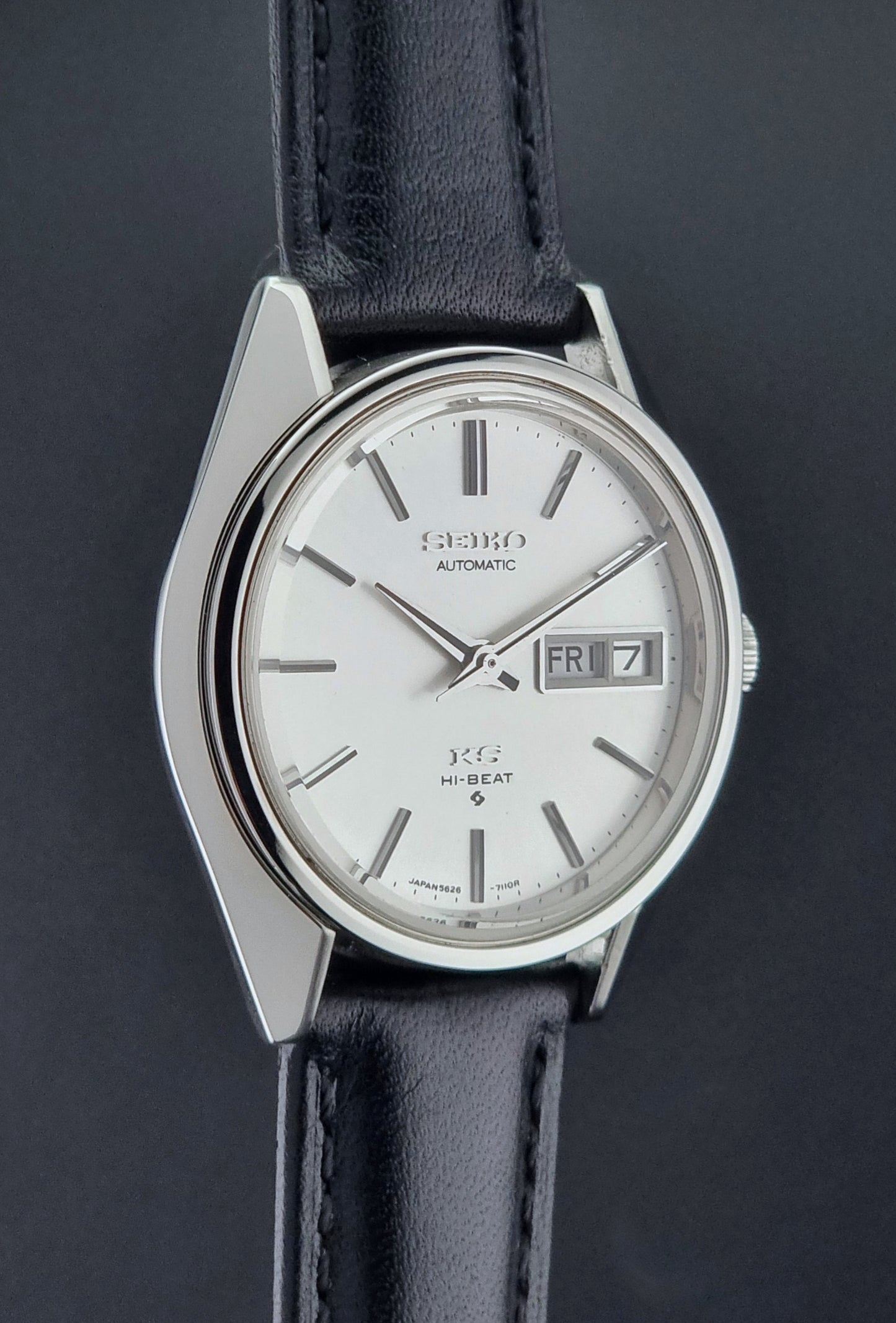 Vintage King Seiko Wristwatch with black leather strap and silver case on a wooden surface side profile