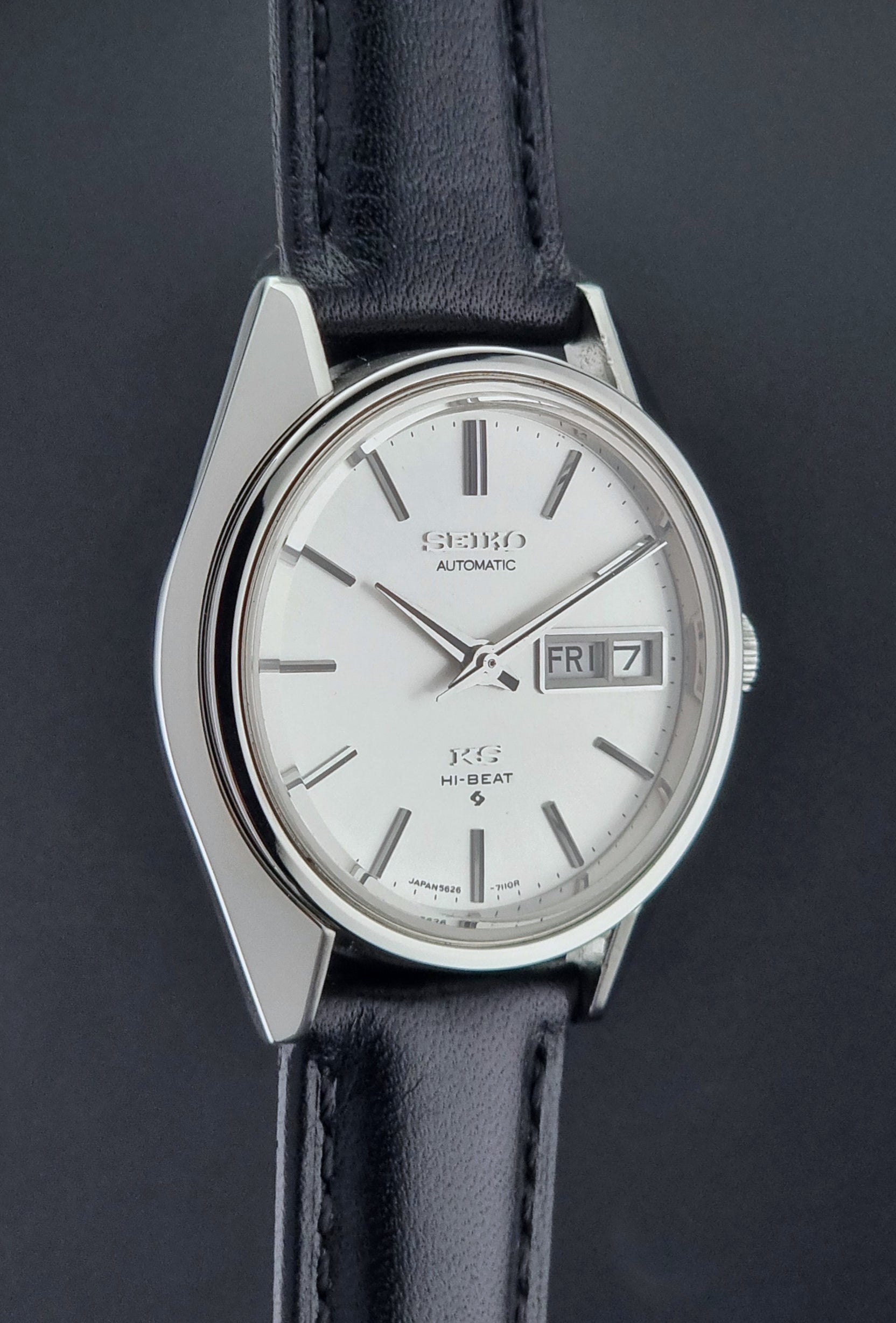 Vintage King Seiko Wristwatch with black leather strap and silver case on a wooden surface side profile