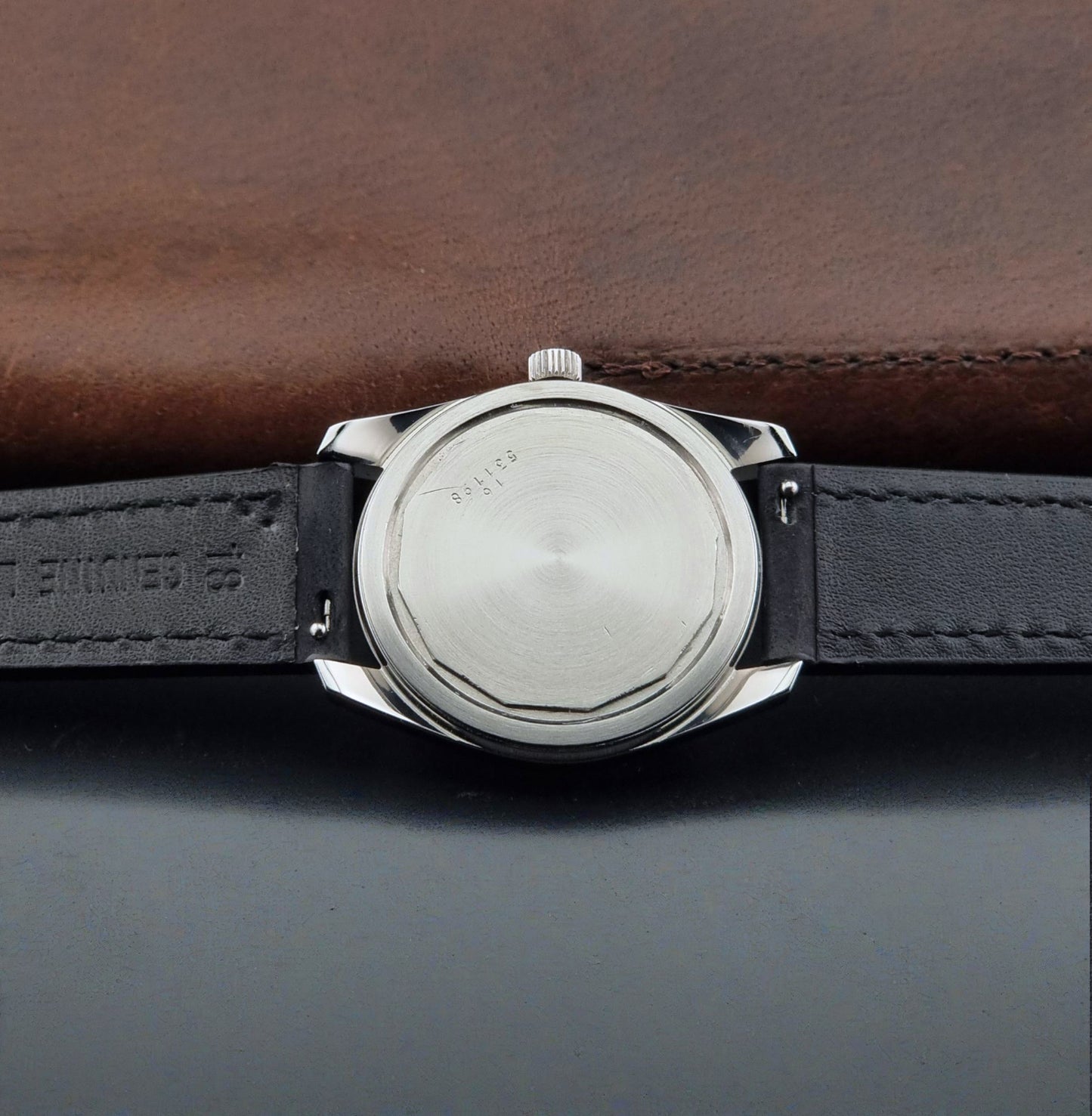 Close-up of the back of A Vintage Longines Admiral HF 2302 Wristwatch and black leather strap, photographed, resting on a dark surface with a brown leather background.