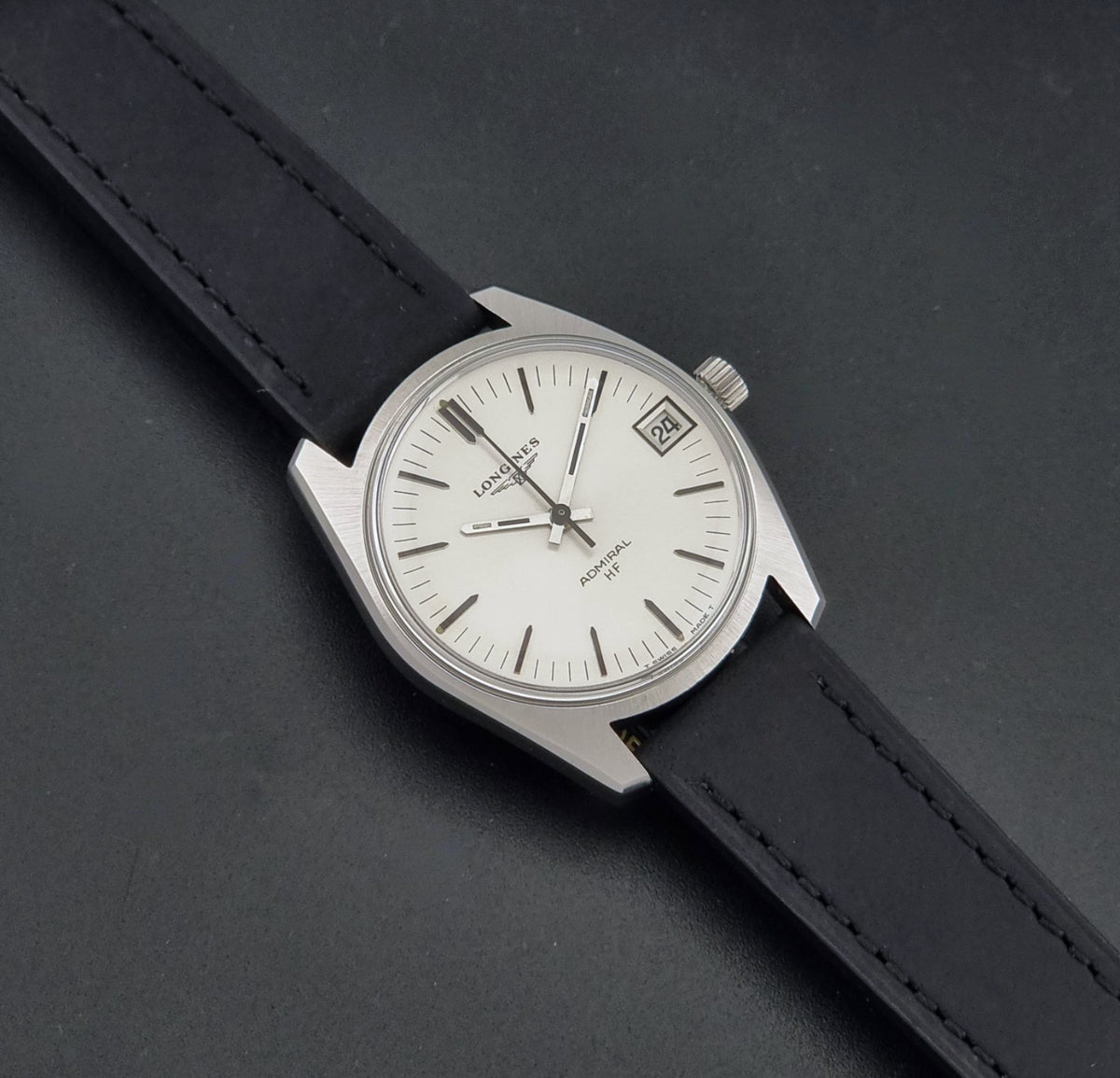 A Vintage Longines Admiral HF 2302 Wristwatch and black leather strap, photographed diagonally on a dark textured background.