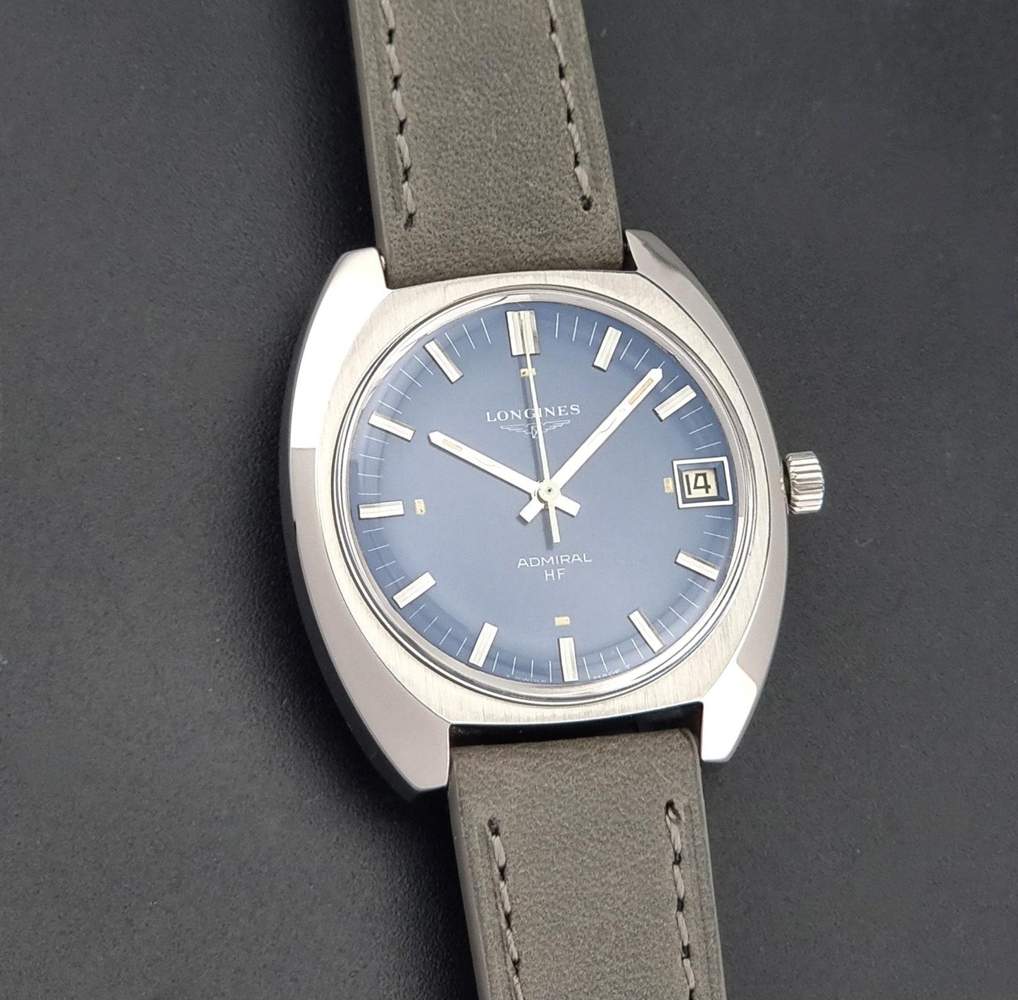 A Vintage Longines Admiral HF 2302 Wristwatch, a blue dial, and a textured gray leather strap, shown on a dark gray background close up view