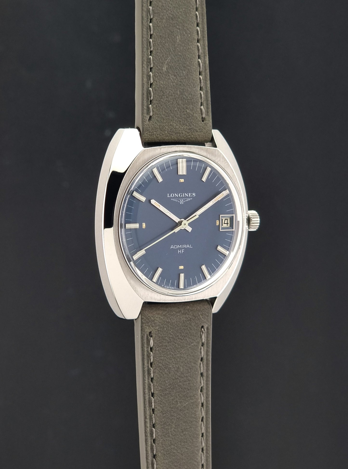 A Vintage Longines Admiral HF 2302 Wristwatch, with a blue dial its side profile shown against a dark gray background. 