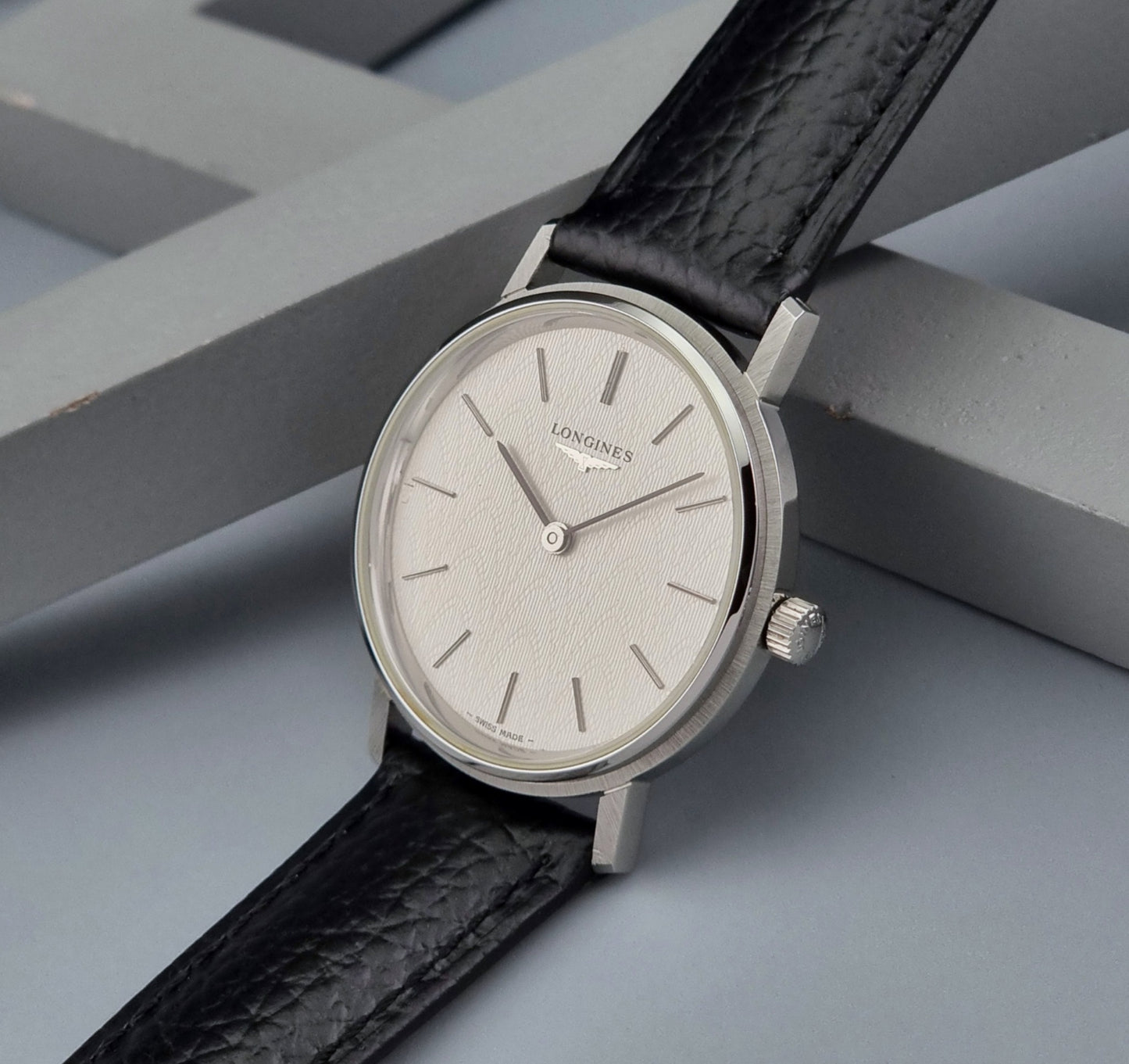 Vintage Longines Wristwatch with black leather strap and silver case on a gray background crown view