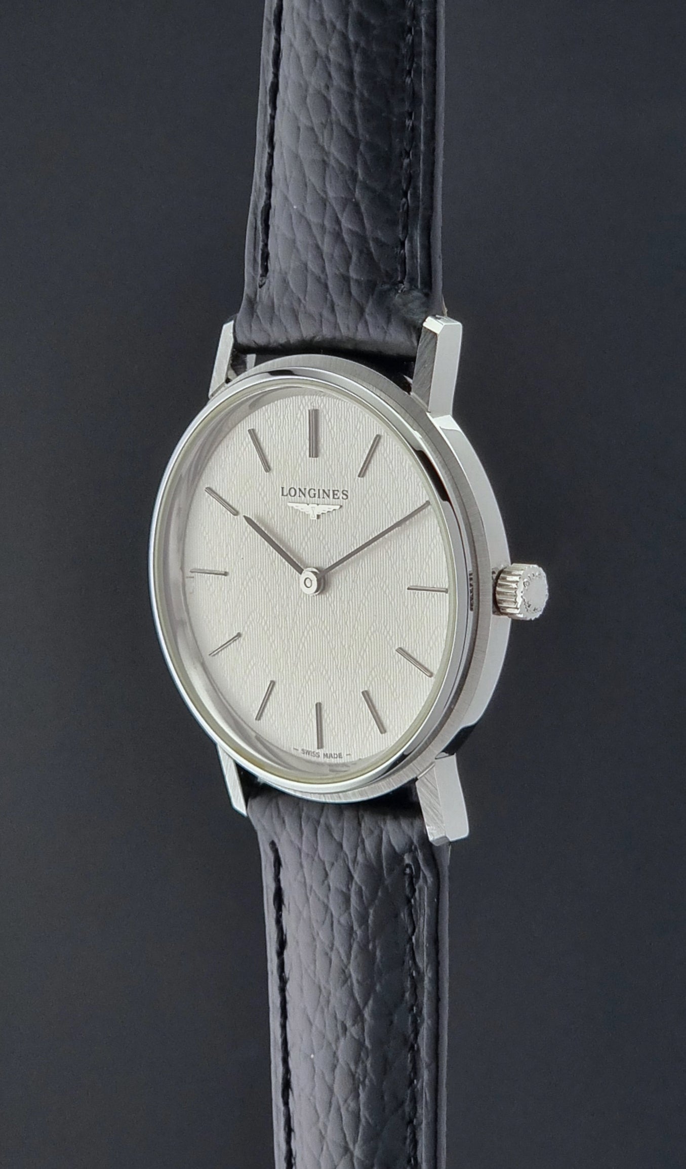 Vintage Longines Wristwatch with black leather strap and silver case on a gray background crown profile view