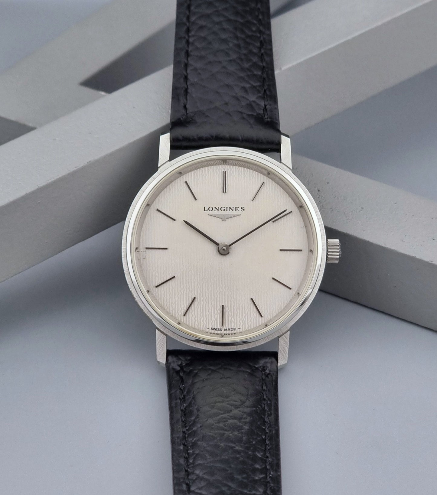 Vintage Longines Wristwatch with black leather strap and silver case on a gray background dial view