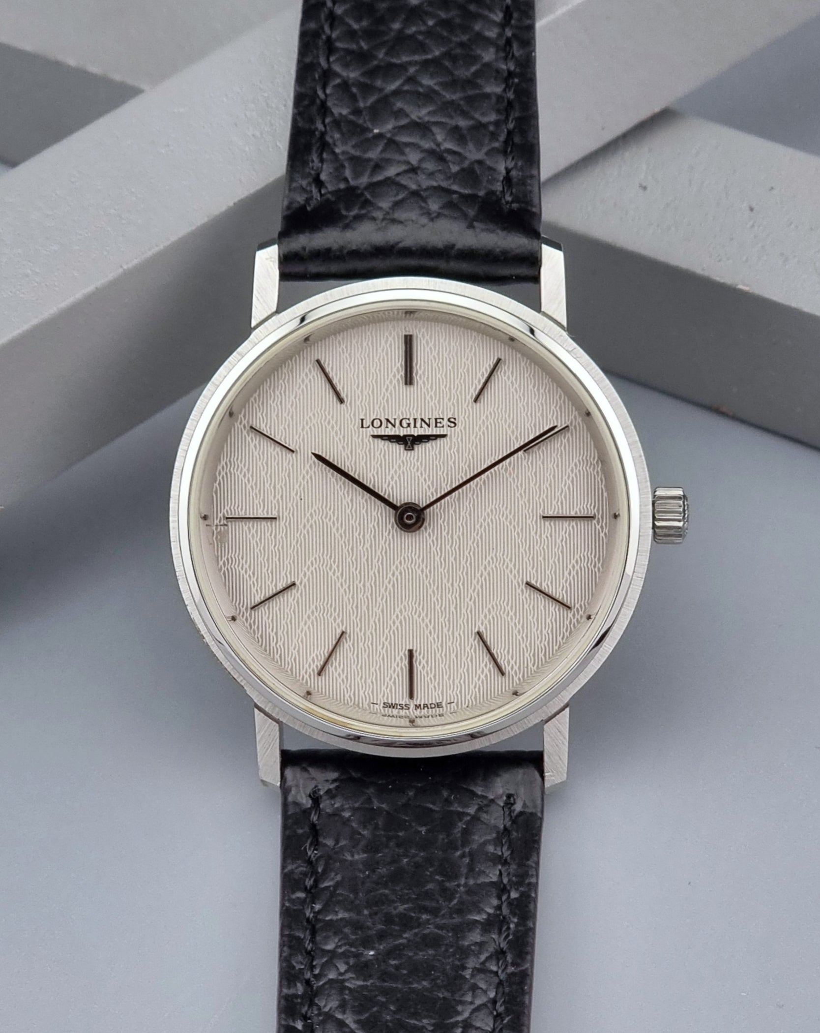 Vintage Longines Wristwatch with black leather strap and silver case on a gray background front view