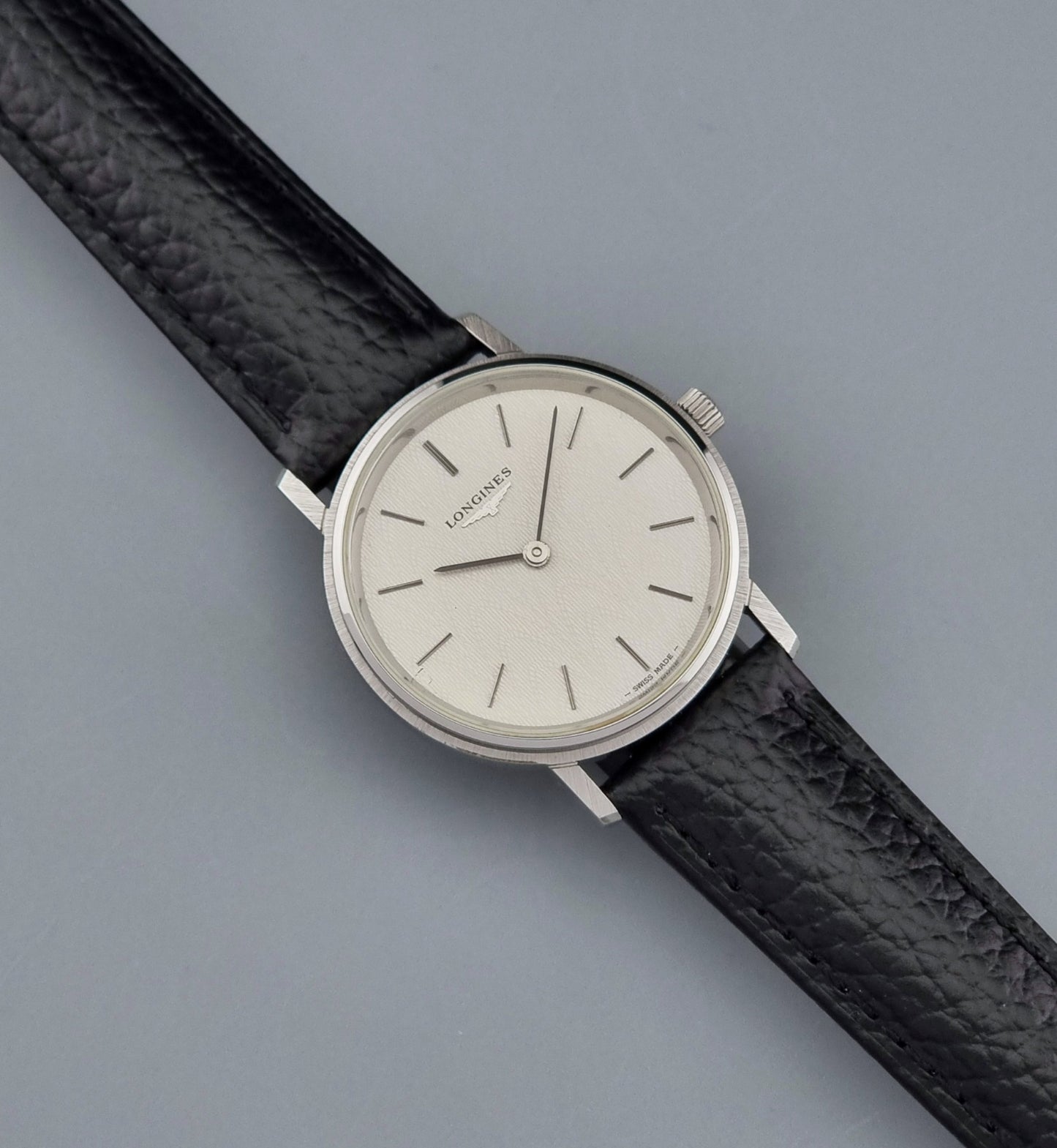 Vintage Longines Wristwatch with black leather strap and silver case on a gray background dial