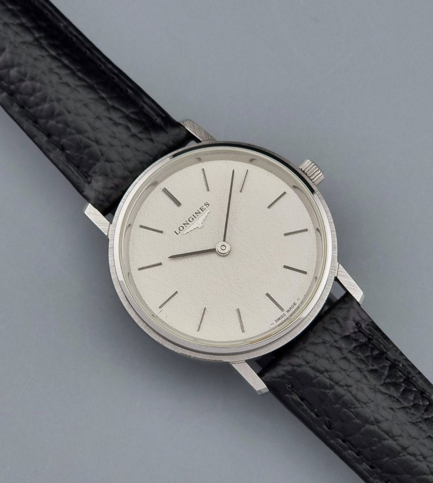 Vintage Longines Wristwatch with black leather strap and silver case on a gray background close up dial view