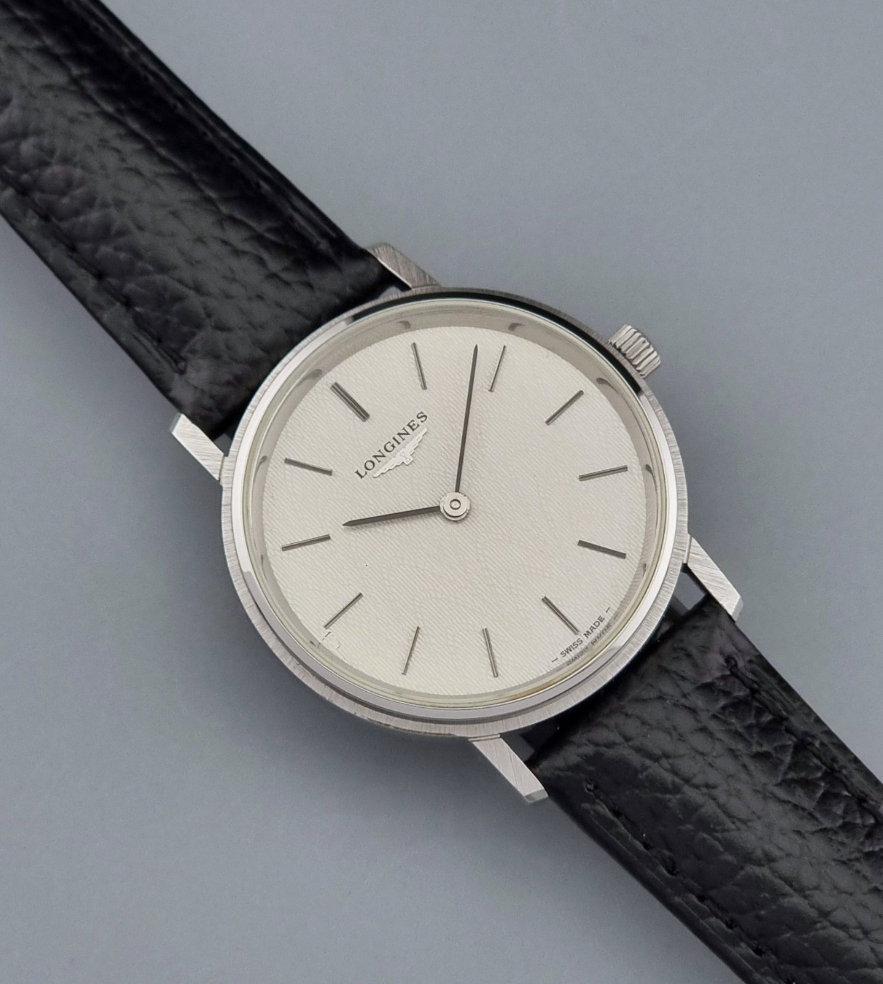 Vintage Longines Wristwatch with black leather strap and silver case on a gray background close up dial view