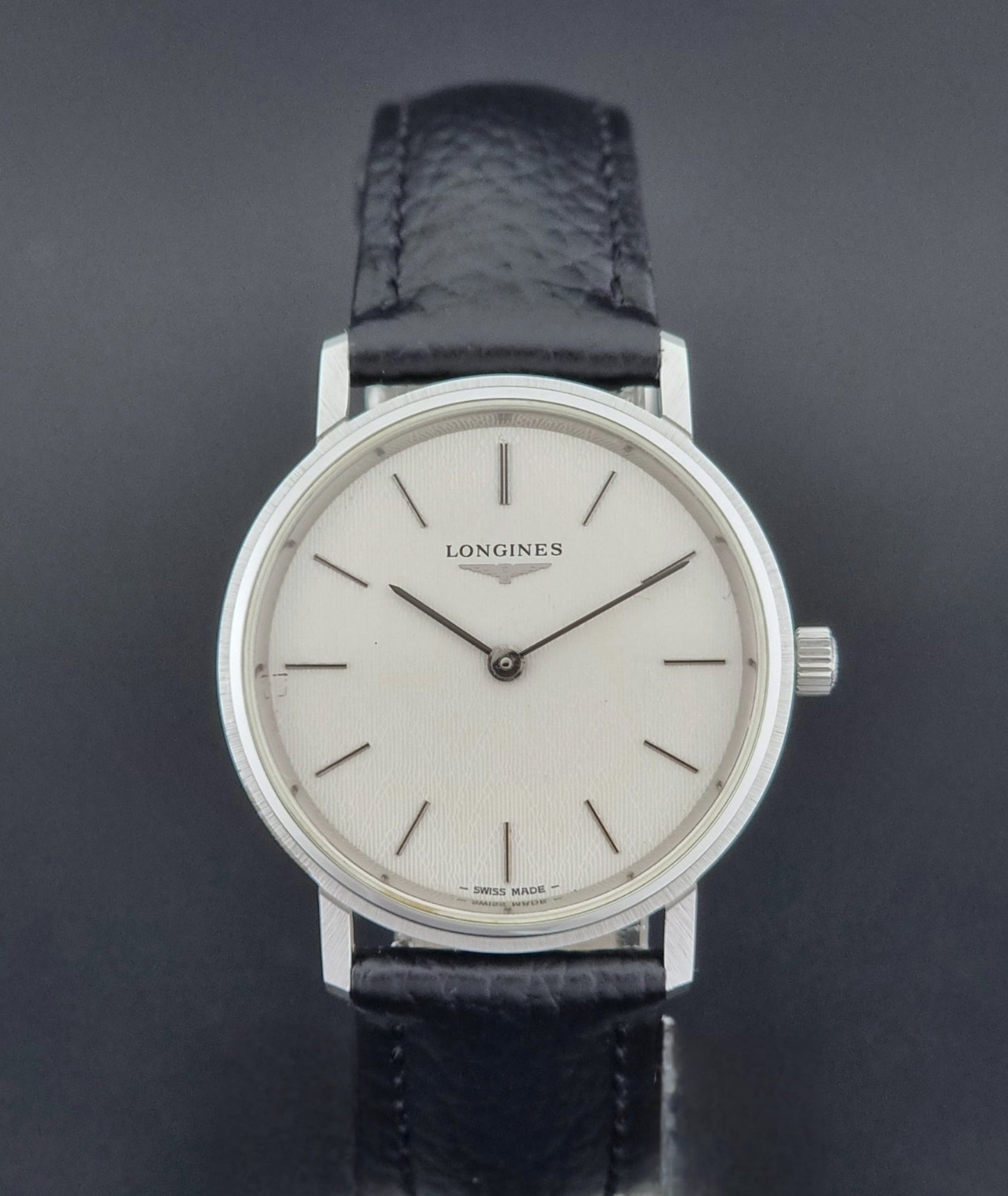 Vintage Longines Wristwatch with black leather strap and silver case on a gray background close dial view