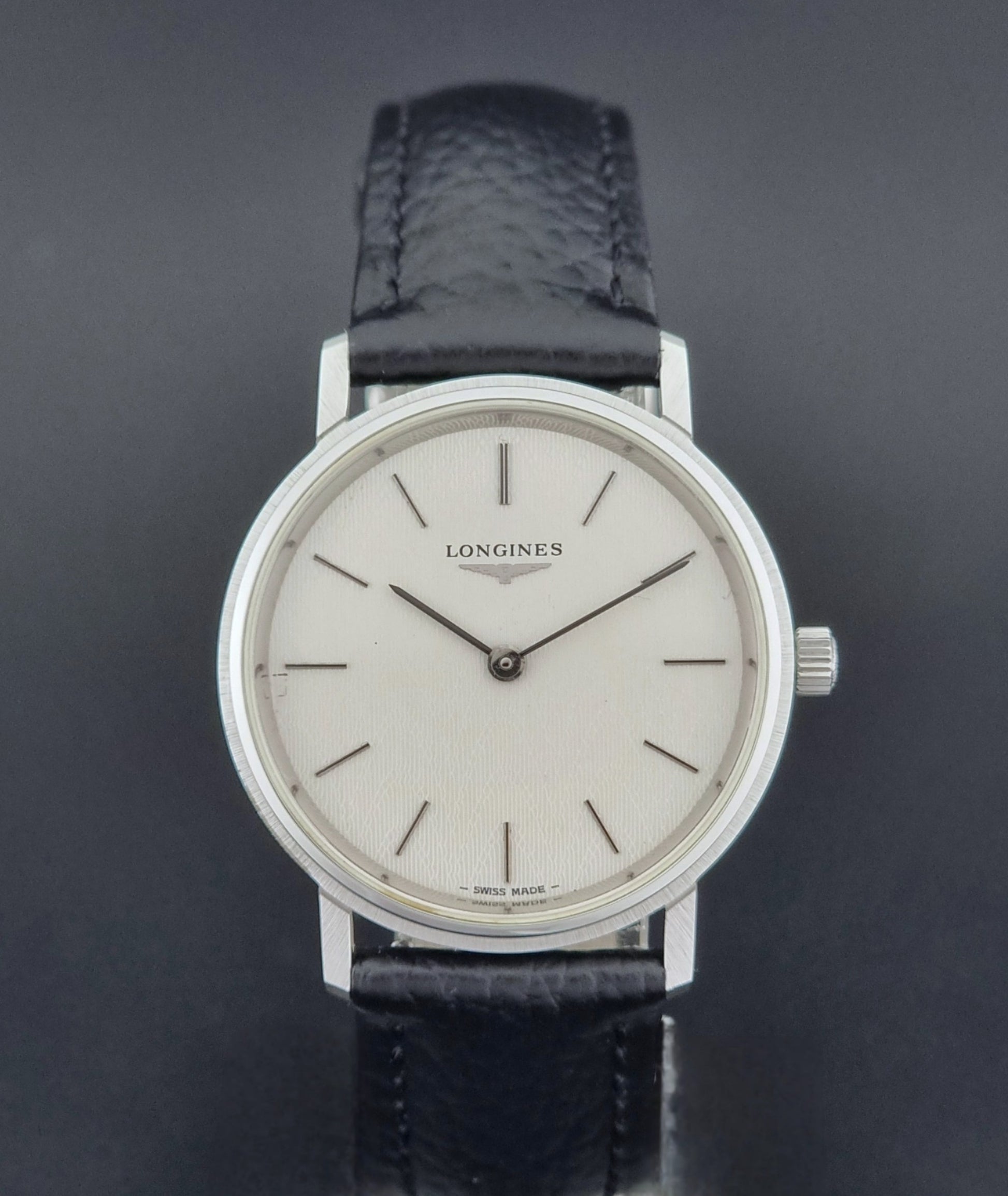 Vintage Longines Wristwatch with black leather strap and silver case on a gray background close dial view