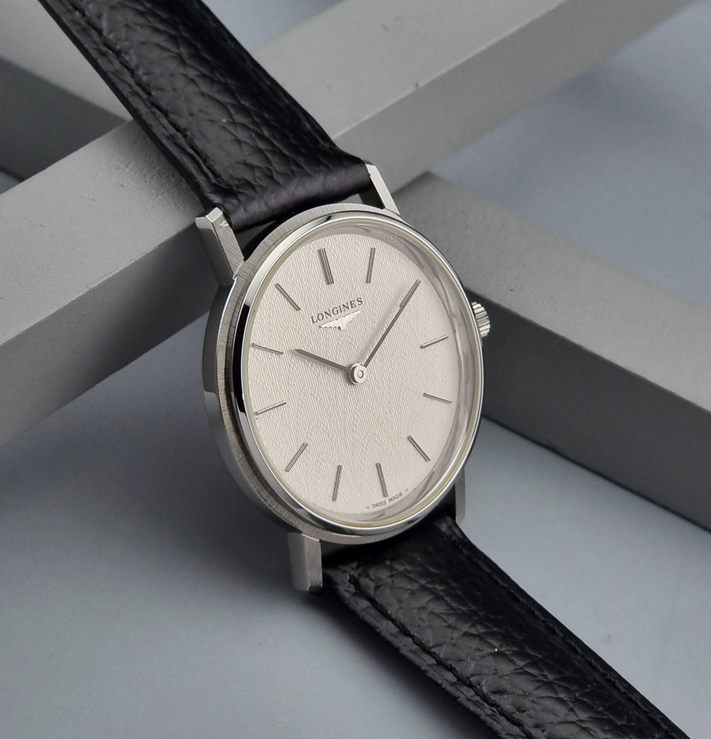 Vintage Longines Wristwatch with black leather strap and silver case on a gray background side view