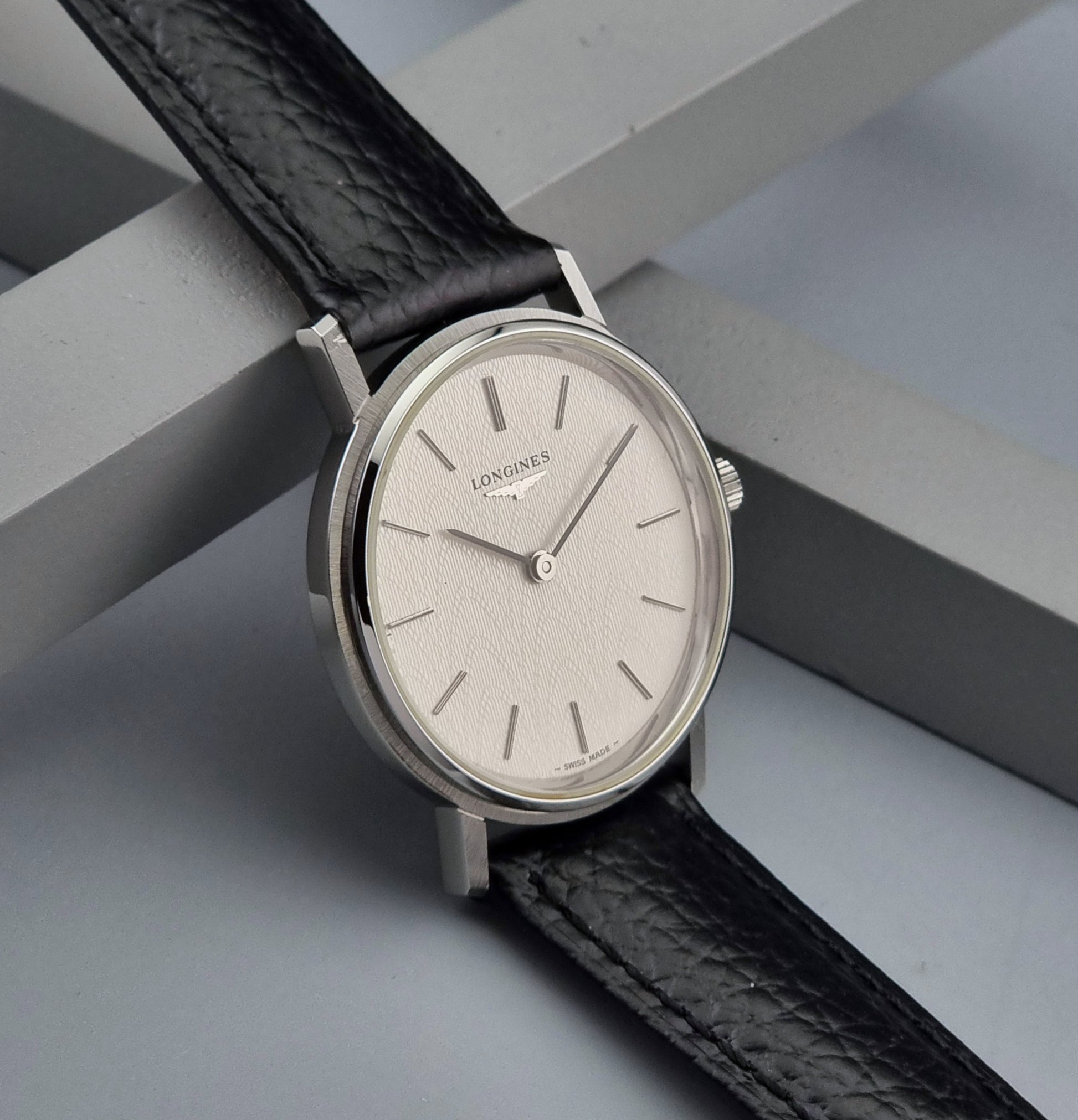 Vintage Longines Wristwatch with black leather strap and silver case on a gray background side view