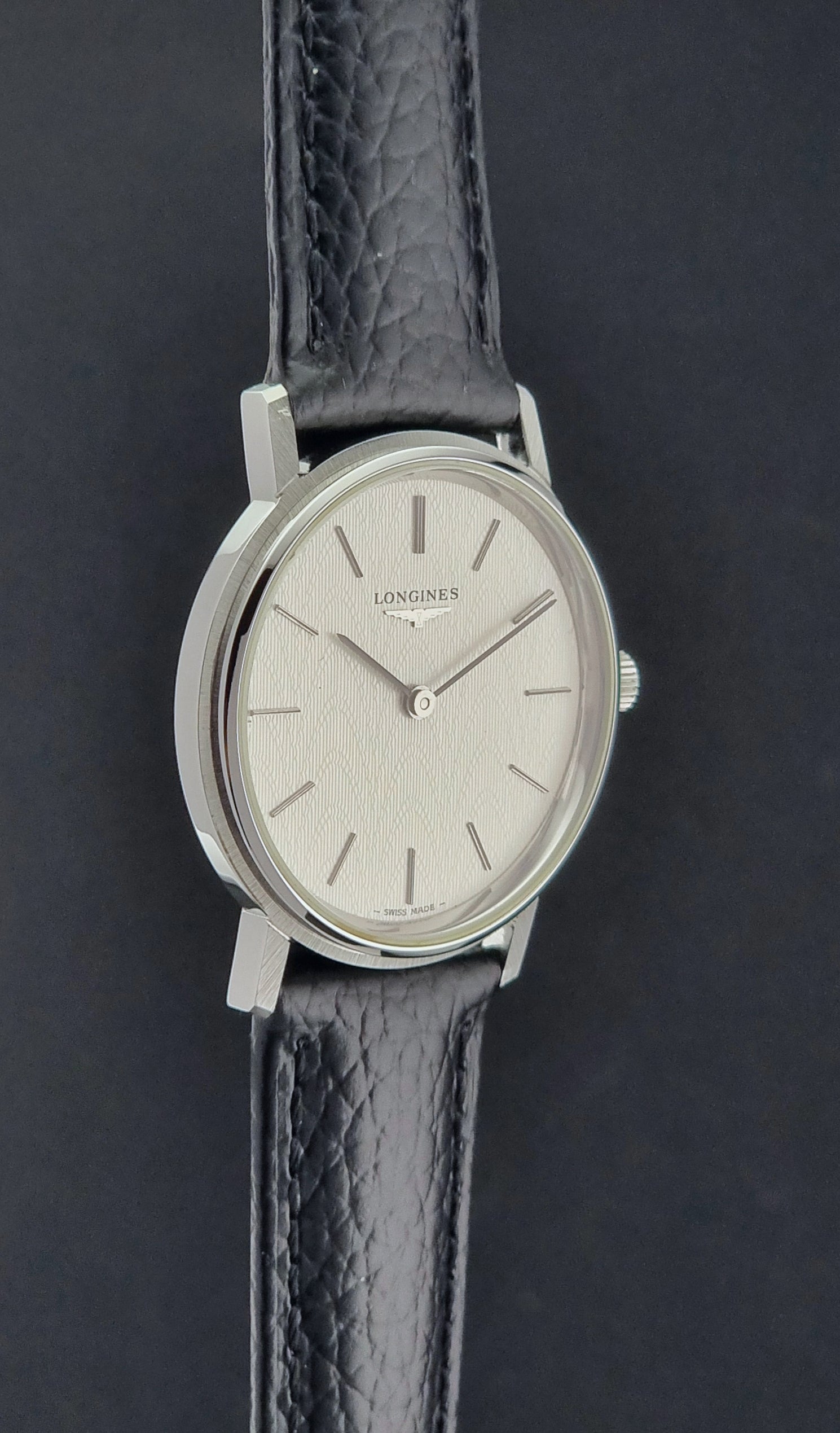 Vintage Longines Wristwatch with black leather strap and silver case on a gray background side profile view