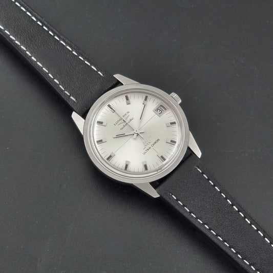 A Vintage Longines ULTRA-CHRON 8309 watch, white dial, and black leather strap with white stitching, photographed on a dark textured background.