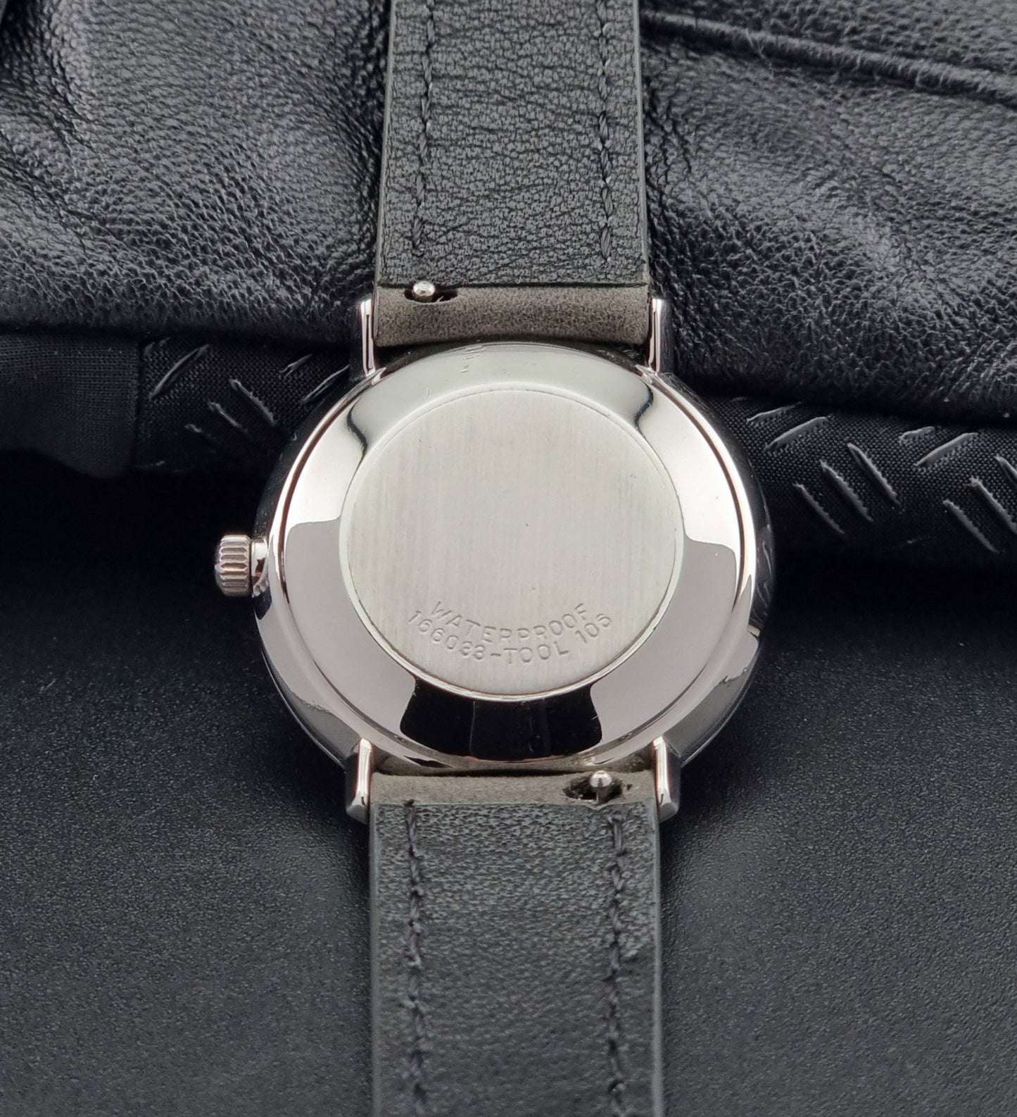 Close-up of a watch back with a gray strap on a dark surface