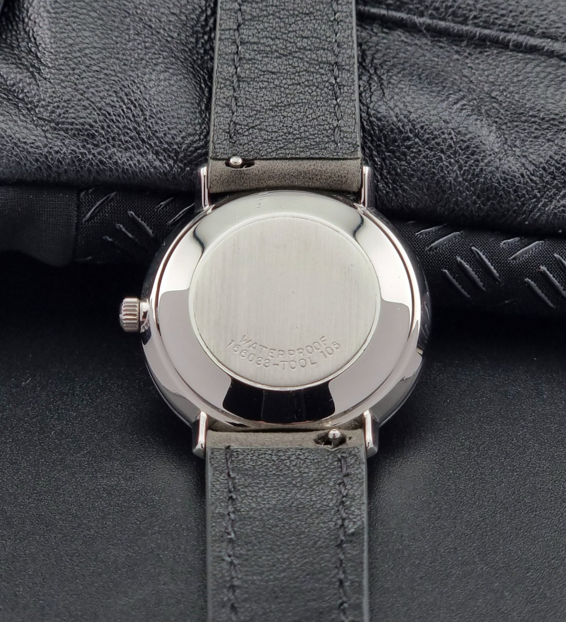Close-up of a watch back with a gray strap on a dark surface