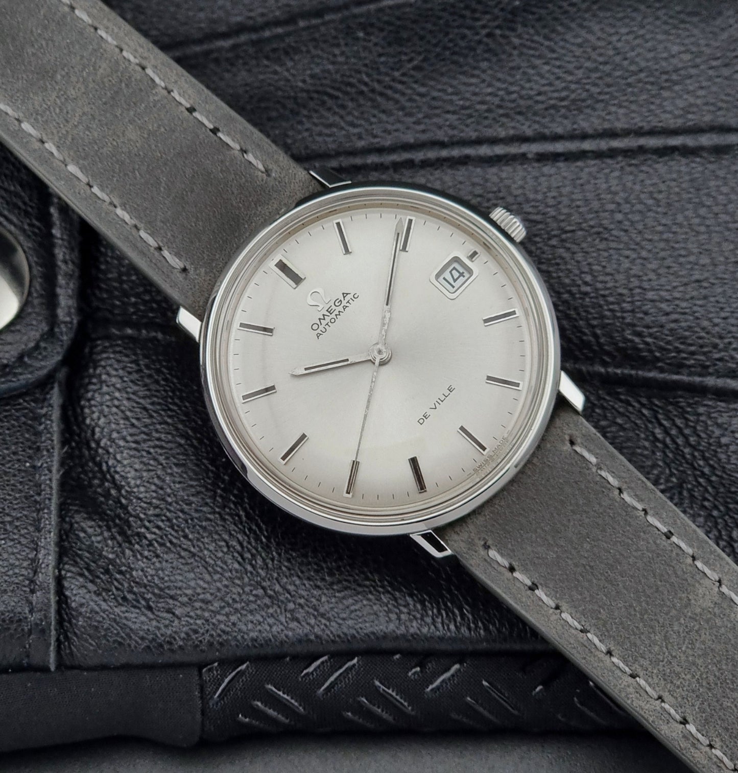 Vintage Omega watch with a silver dial and gray leather strap on a textured black surface