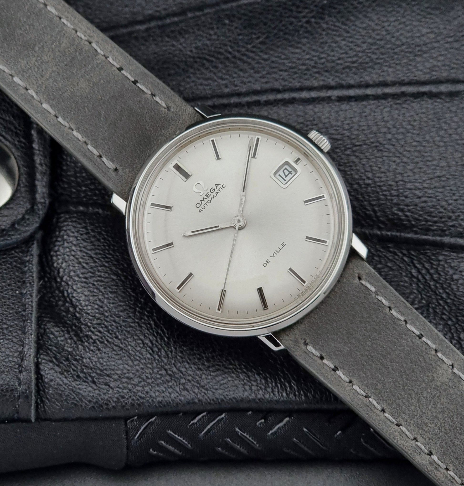 Vintage Omega watch with a silver dial and gray leather strap on a textured black surface