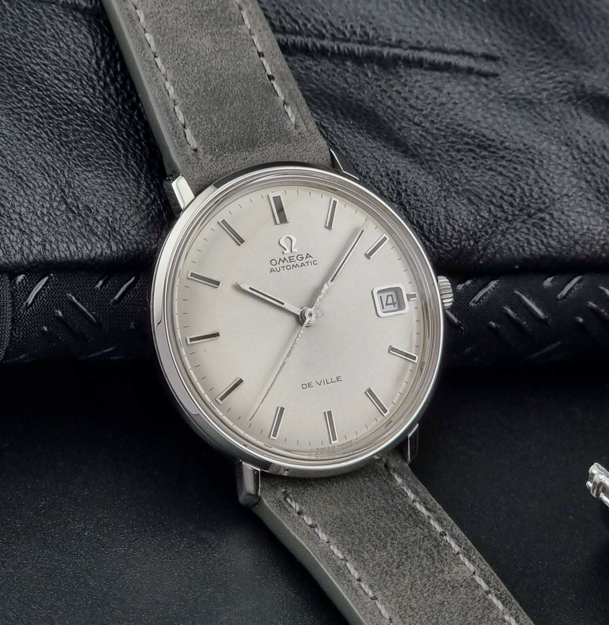 Omega watch with a silver dial and gray leather strap on a textured black background