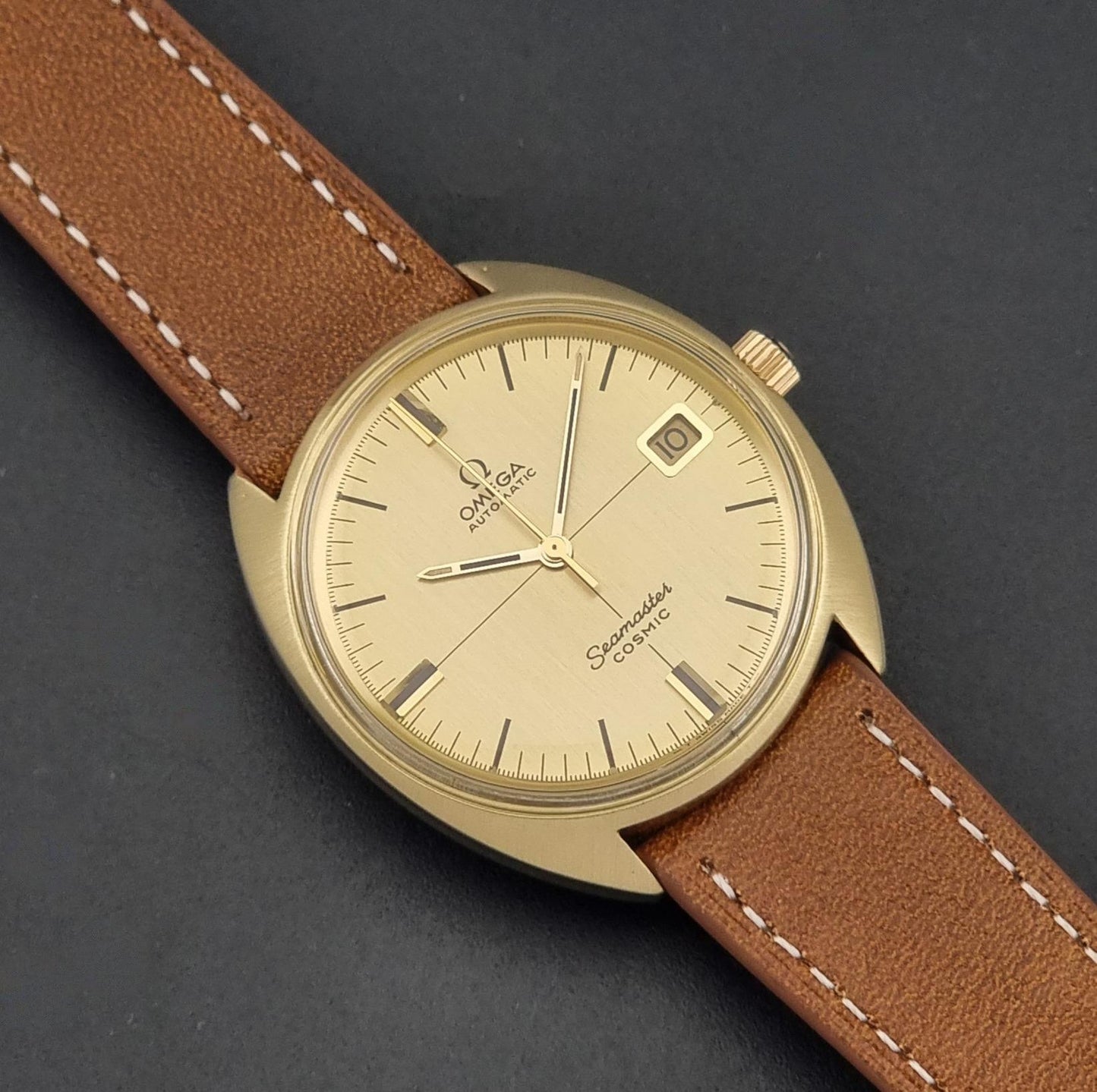 A Vintage Omega 166.026 Seamaster Cosmic Automatic Gold Capped watch on a dark background close up of the dial