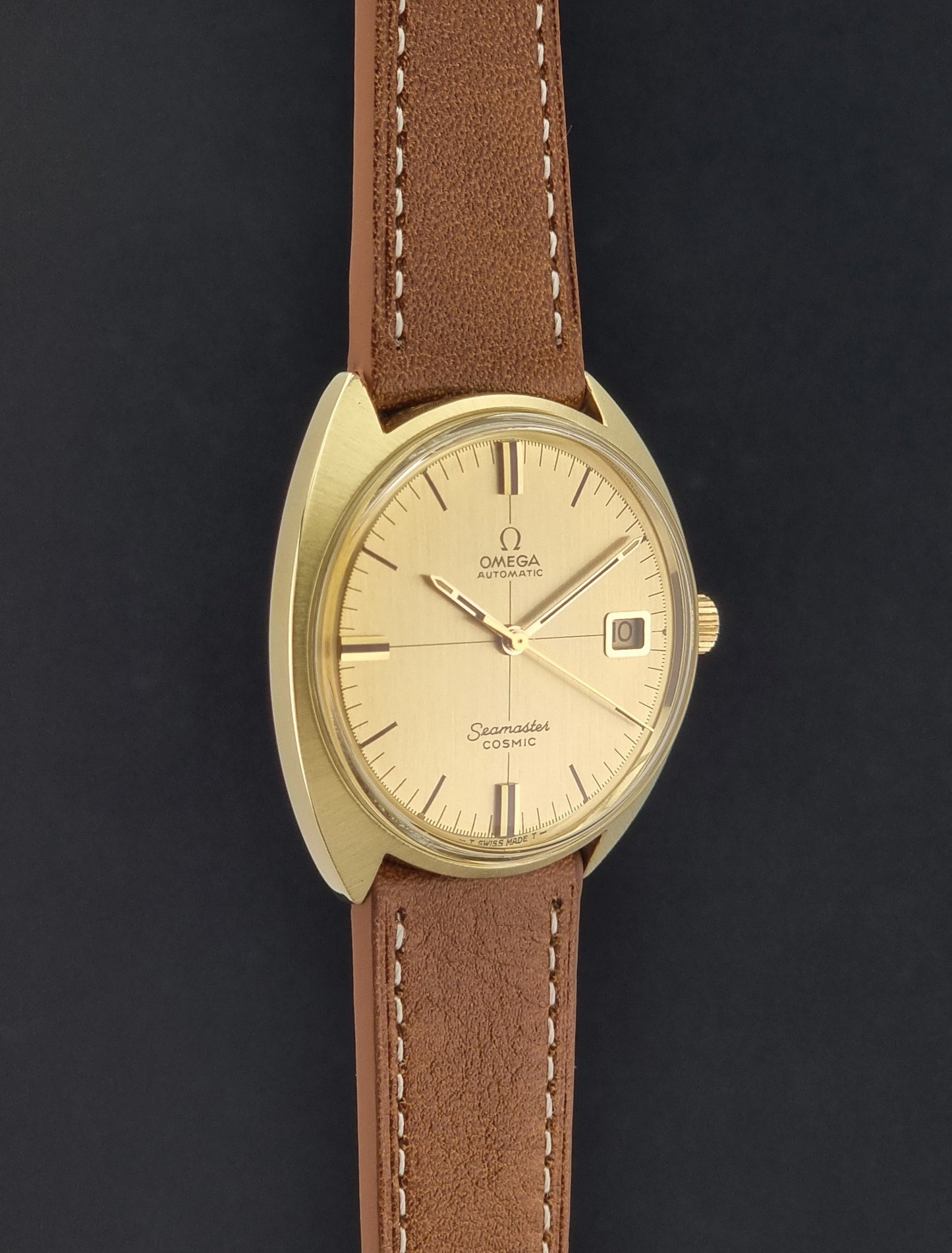 A Vintage Omega 166.026 Seamaster Cosmic Automatic Gold Capped watch on a dark background l, and a brown leather strap with white stitching