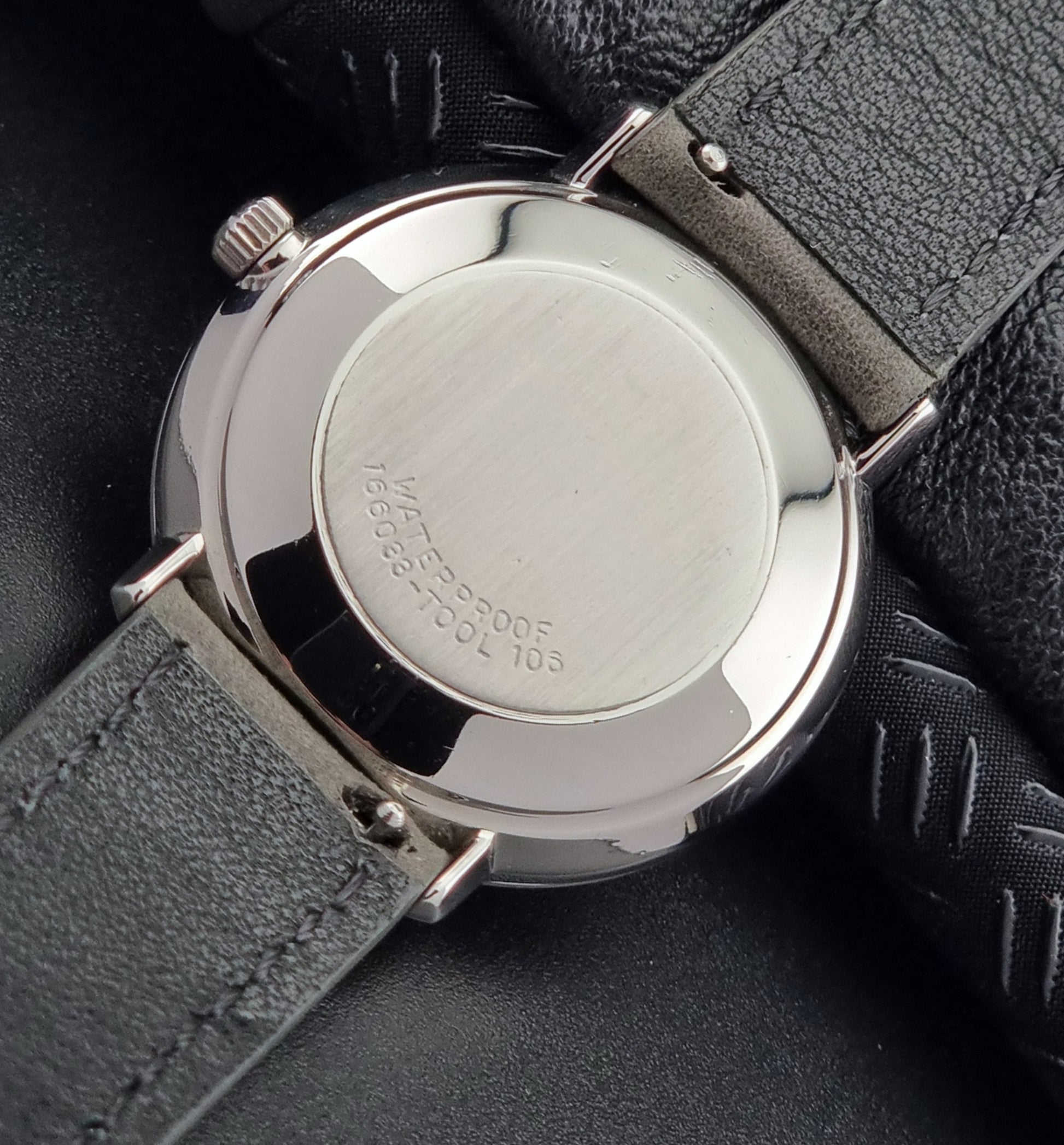 Close-up of an Omega watch back with a silver case and black leather strap on a dark background