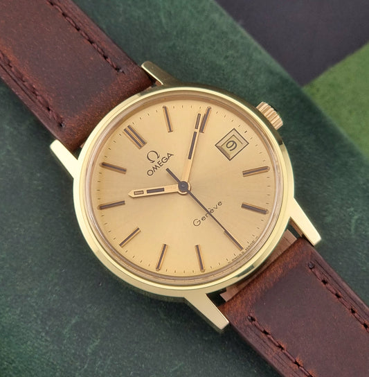 Vintage Gold Omega Geneve watch with brown leather strap on a green surface