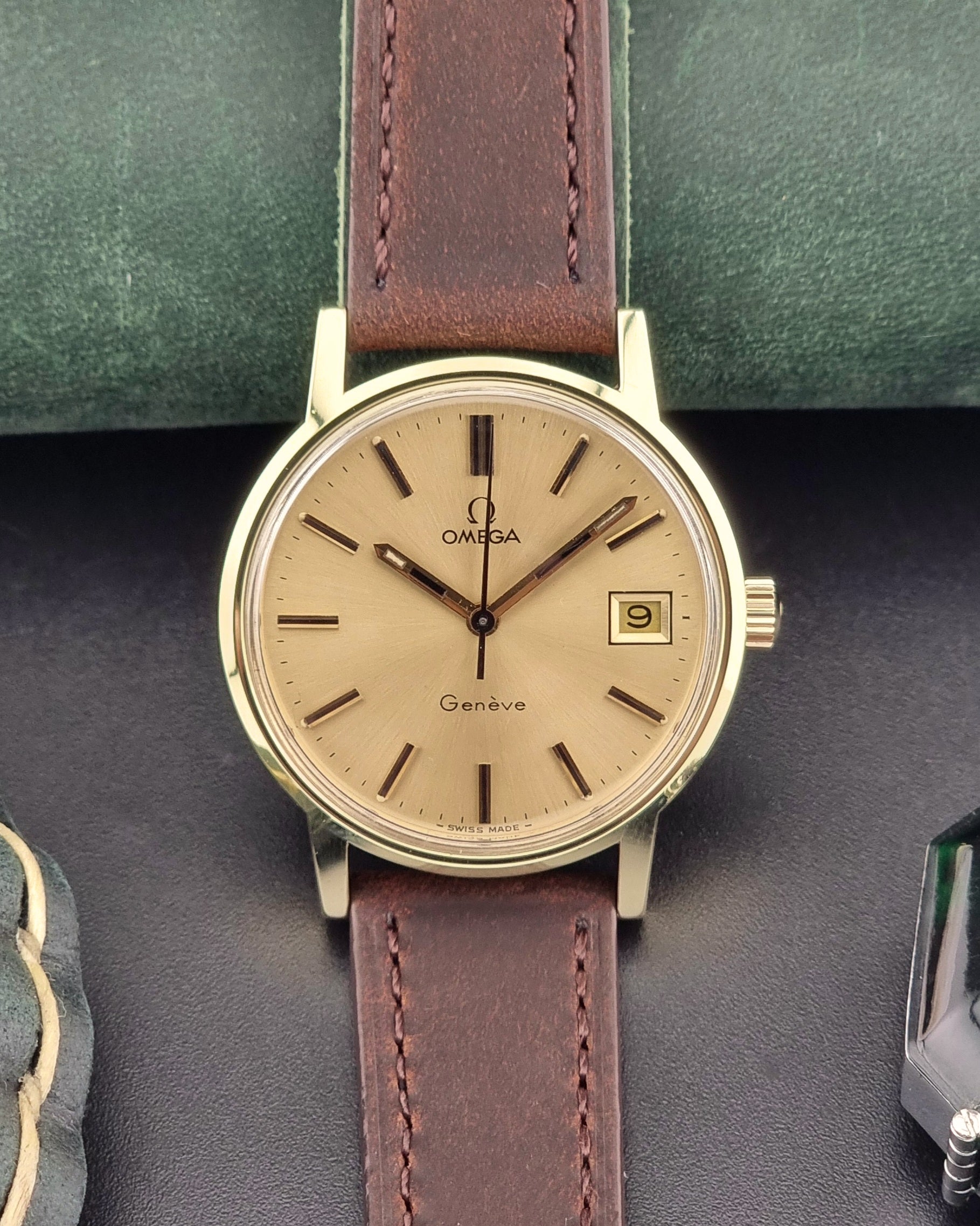 Vintage Gold Omega Geneve watch with brown leather strap on a dark surface