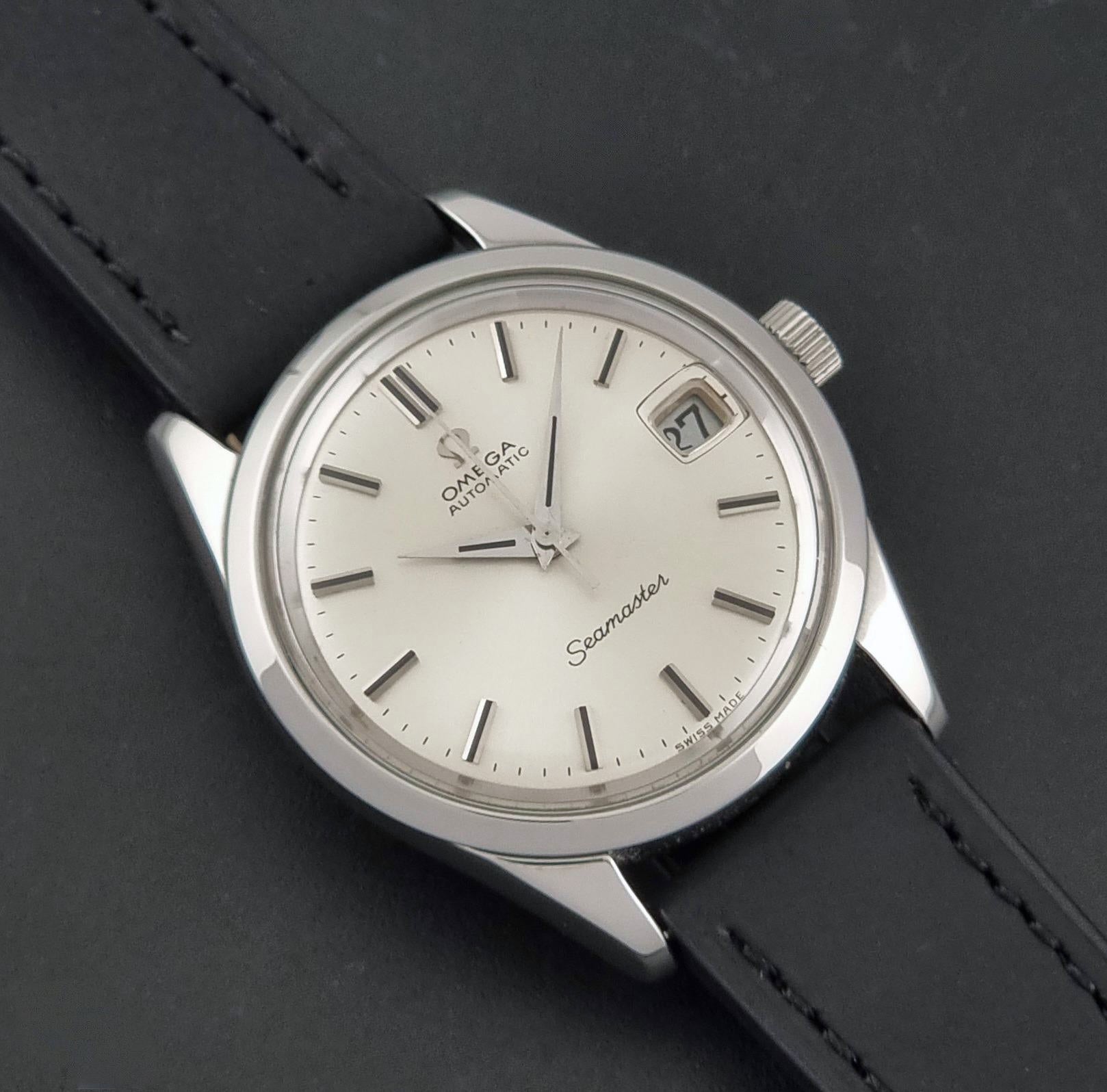A vintage Omega Seamaster wristwatch with a silver-toned metal case, white dial, and black leather strap, shown diagonally on a dark textured background.