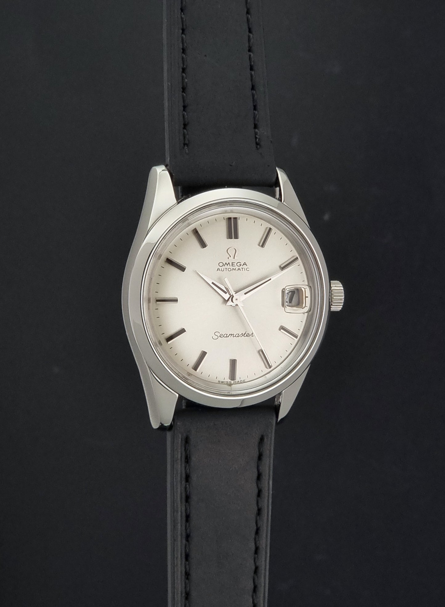 An Omega Seamaster wristwatch with a silver-toned stainless steel case, white dial, and a black leather strap, shown against a dark background.