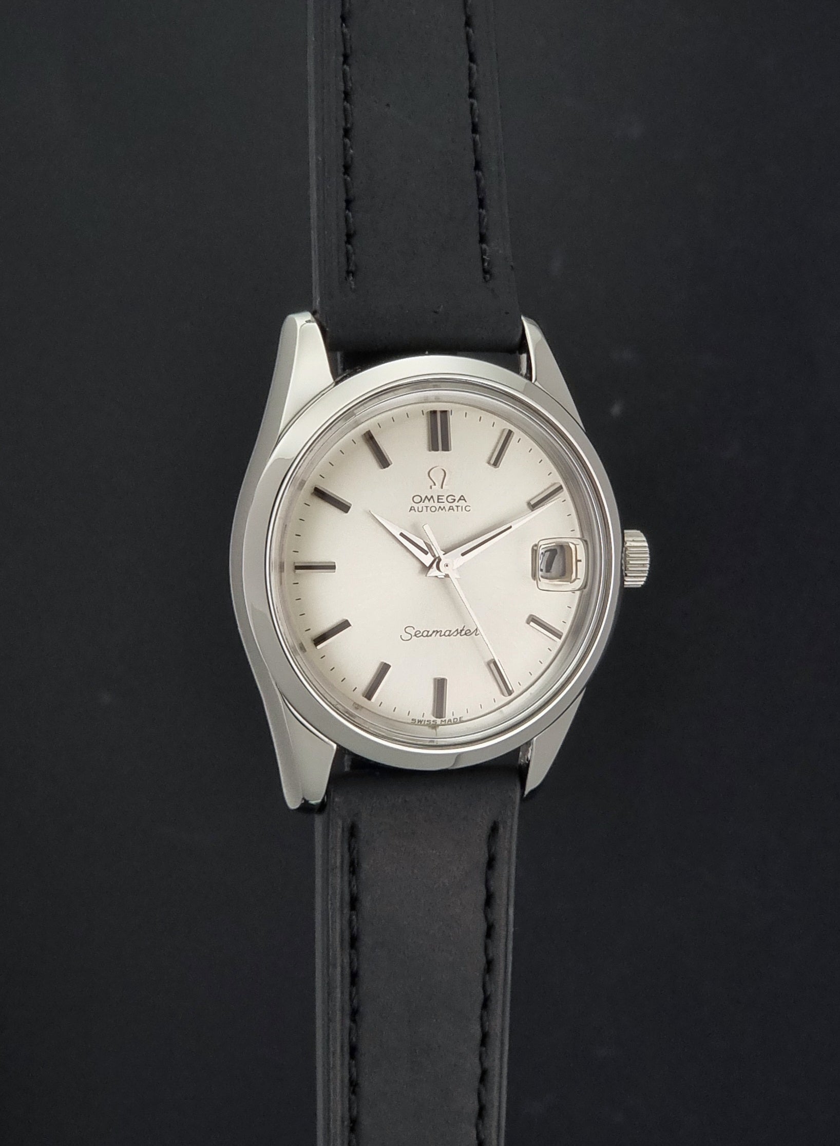 An Omega Seamaster wristwatch with a silver-toned stainless steel case, white dial, and a black leather strap, shown against a dark background.