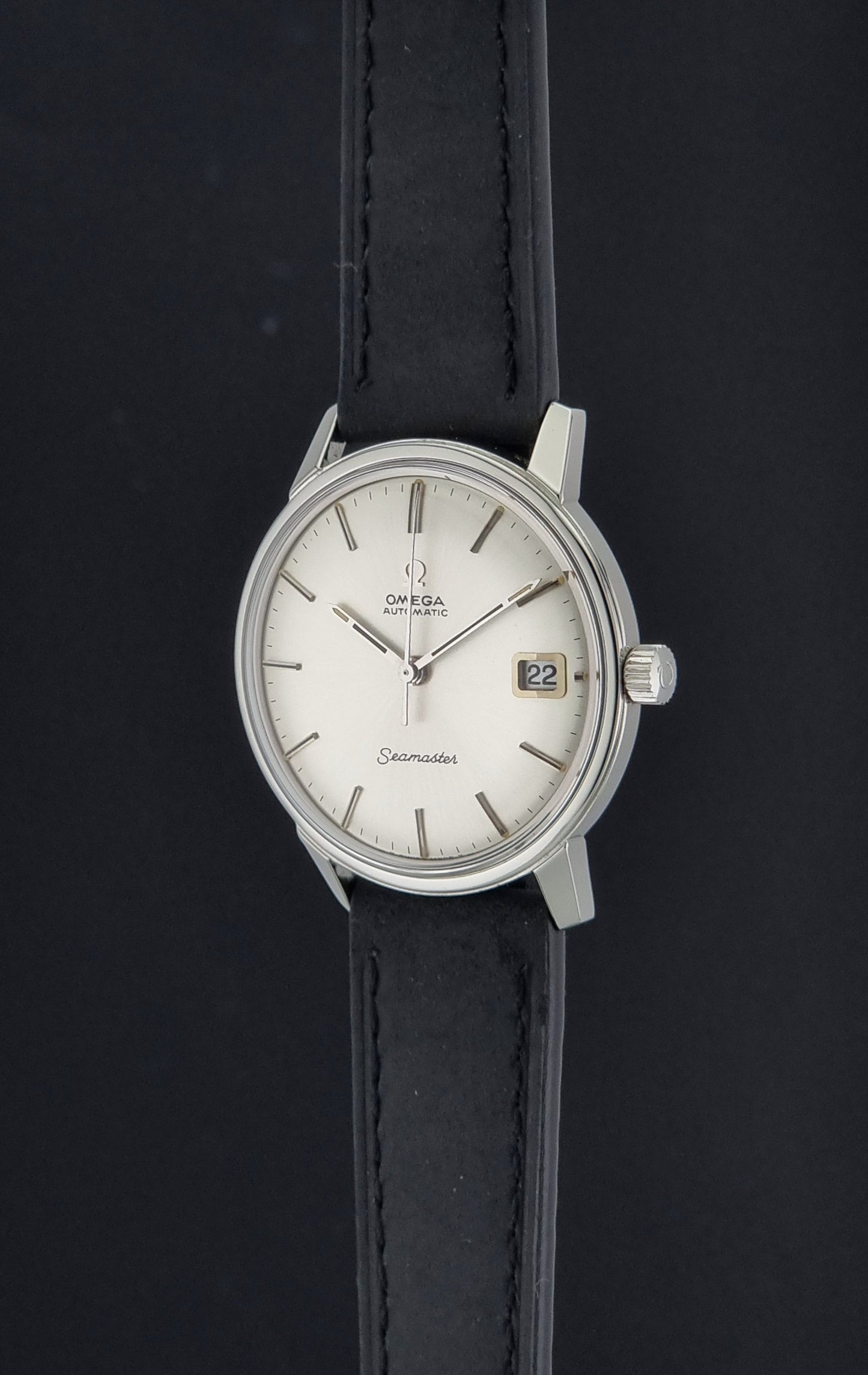 An Omega Seamaster wristwatch with a silver-toned stainless steel case, white dial, and black leather strap, shown against a dark background.