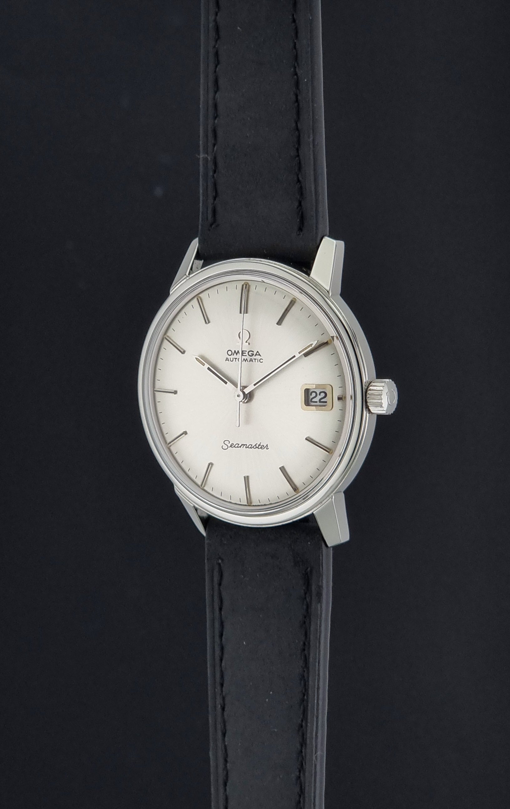 An Omega Seamaster wristwatch with a silver-toned stainless steel case, white dial, and black leather strap, shown against a dark background.