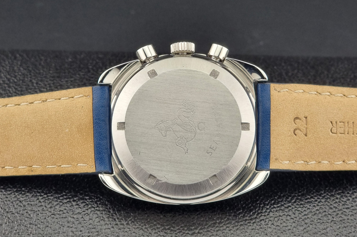 Close-up of a watch case back with a  leather strap on a dark background
