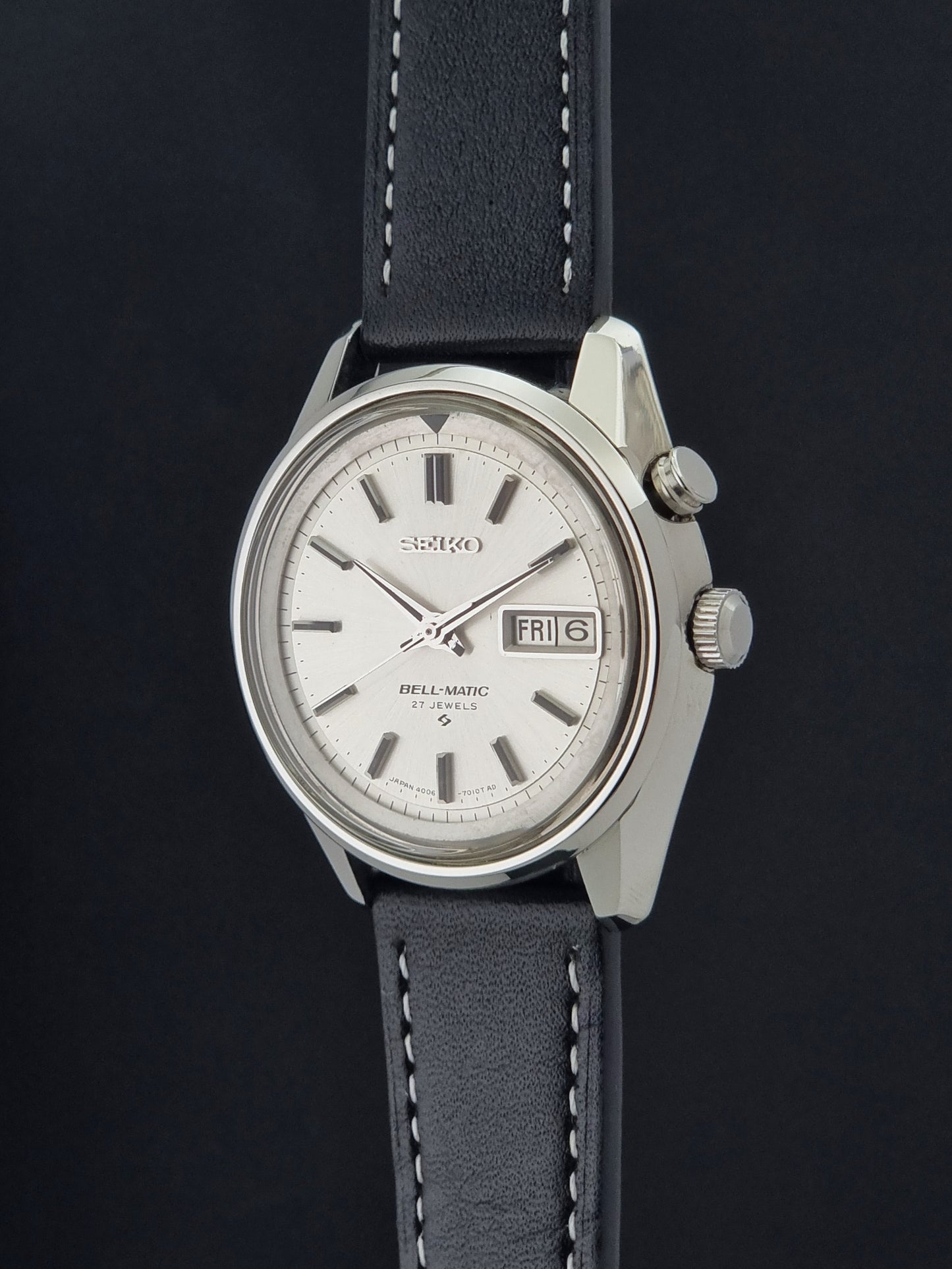 A vintage Seiko Bellamatic watch with a silver-toned metal case, white dial, and a dark gray leather strap with white stitching, shown against a dark background.