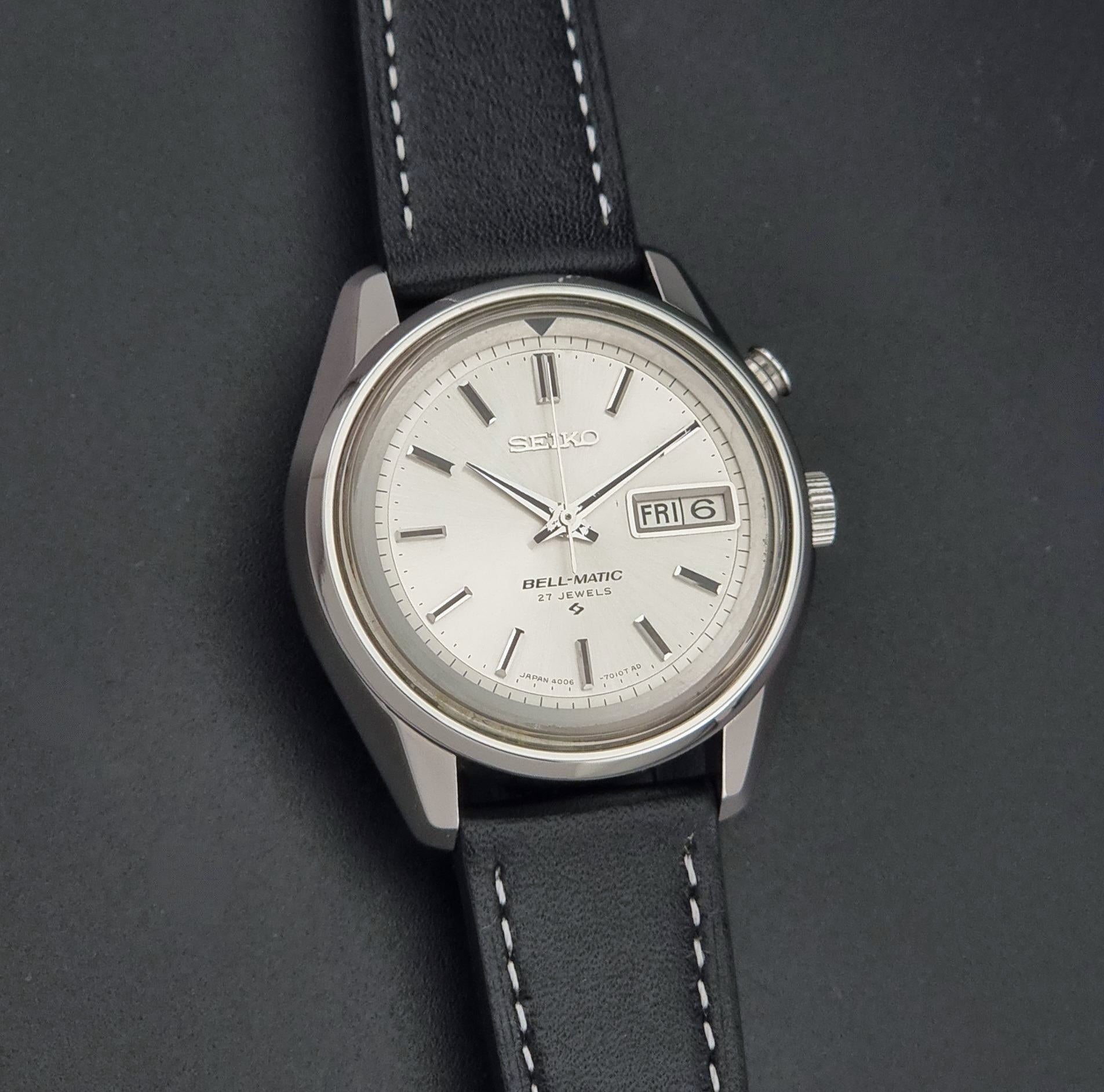 Vintage Seiko Wristwatch Bell Matic Alarm 4006-7010, a white dial with black stick indices, and a black leather strap with white stitching, shown on a dark background.