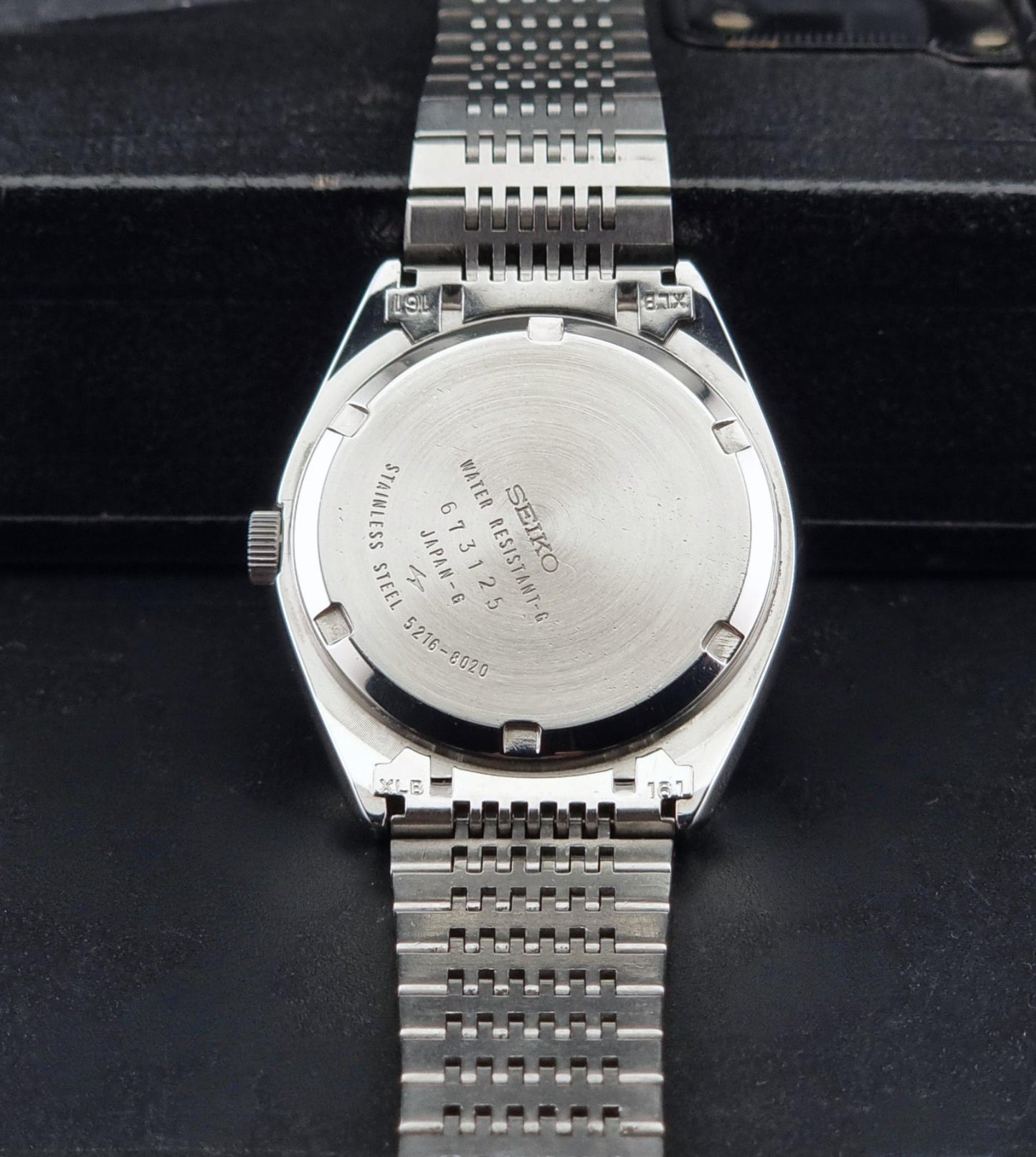 The back of a Vintage Seiko LordMatic Special 5216-8020 Wristwatch, resting on a black textured surface.