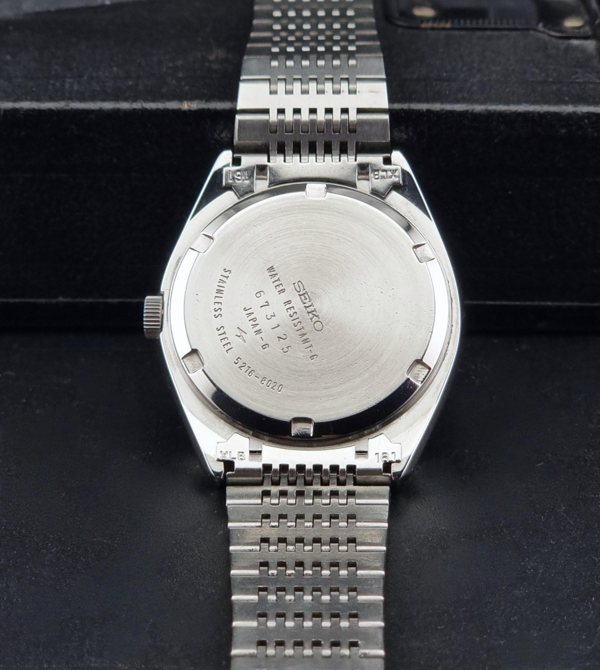 The back of a Vintage Seiko LordMatic Special 5216-8020 Wristwatch, resting on a black textured surface.