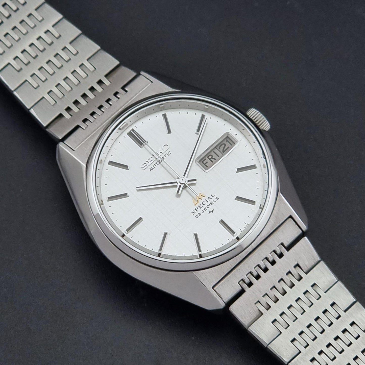 A Vintage Seiko LordMatic Special 5216-8020 Wristwatch with a silver stainless steel case and integrated link bracelet, featuring a white dial with silver hour markers and a day window showing Friday.