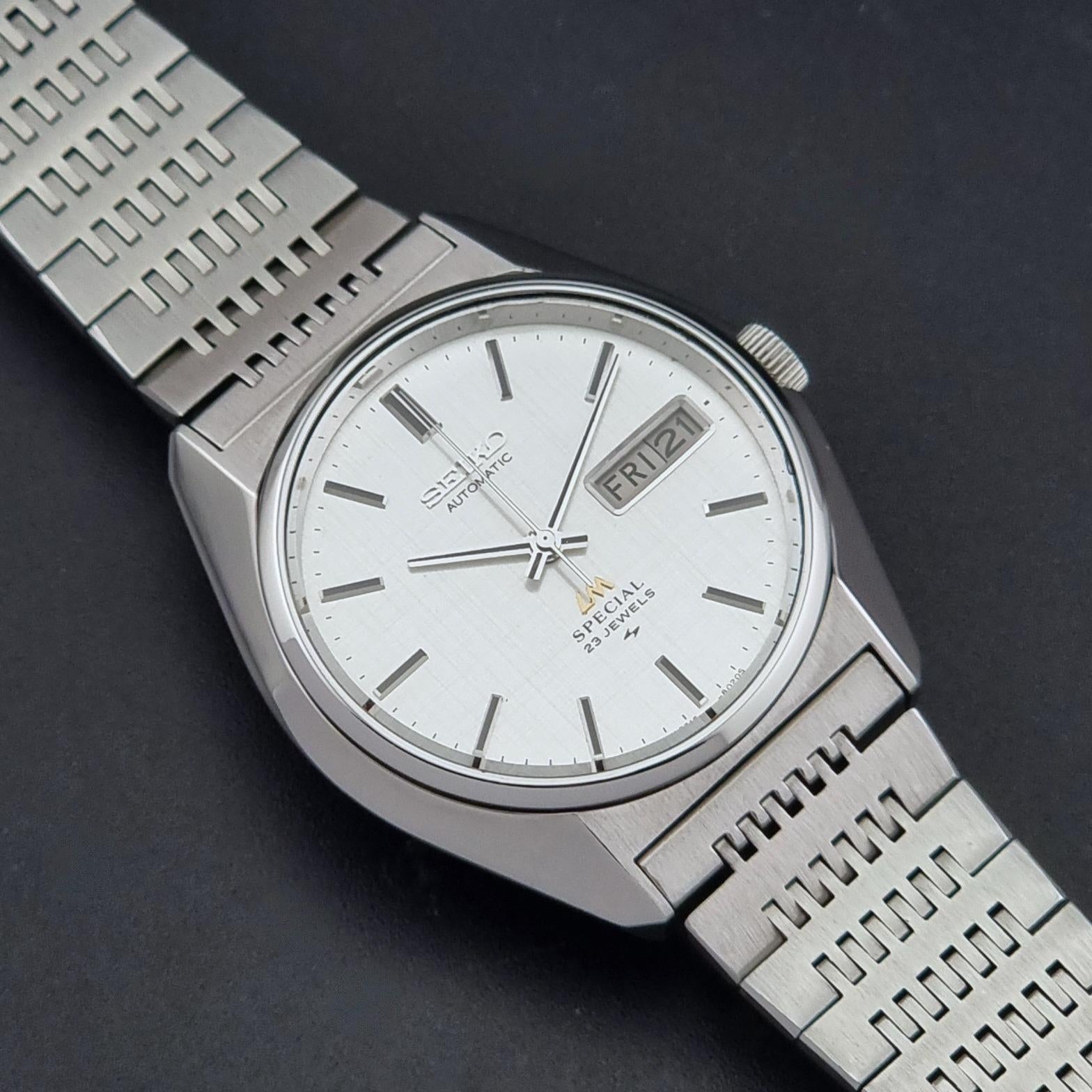 A Vintage Seiko LordMatic Special 5216-8020 Wristwatch with a silver stainless steel case and integrated link bracelet, featuring a white dial with silver hour markers and a day window showing Friday.