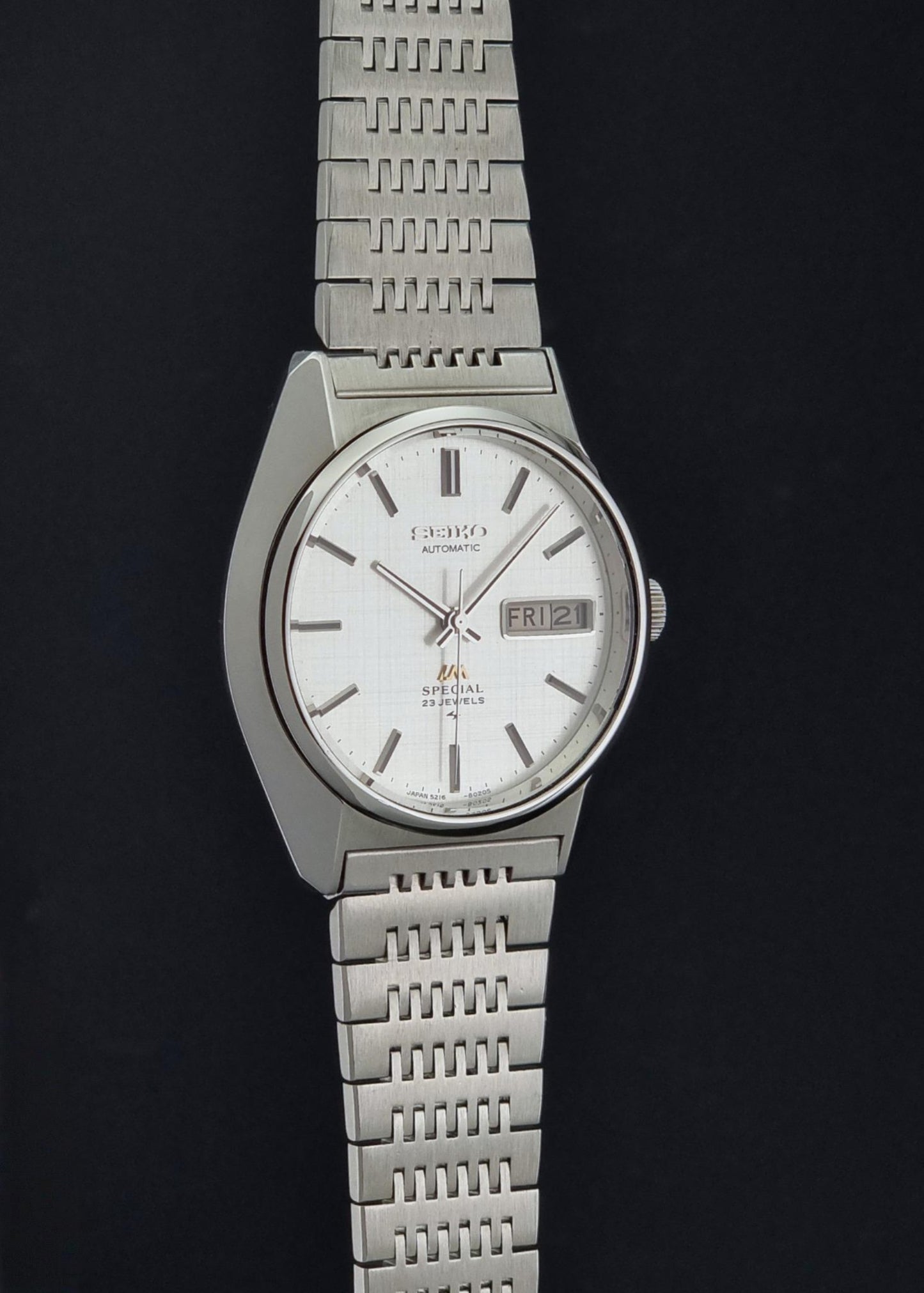 A Vintage Seiko LordMatic Special 5216-8020 Wristwatch with a silver-toned metal link bracelet and a white dial, shown against a solid black background.