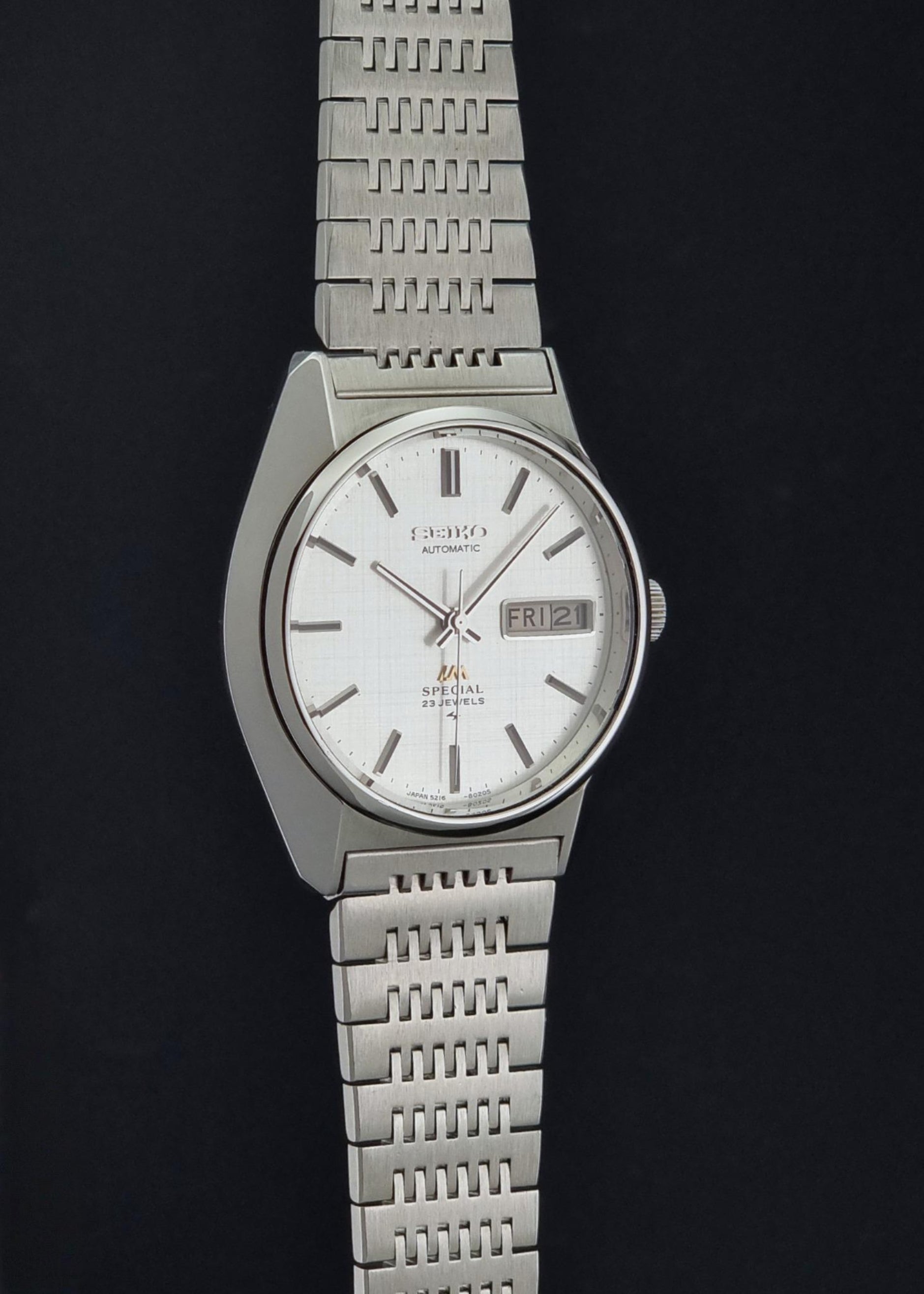 A Vintage Seiko LordMatic Special 5216-8020 Wristwatch with a silver-toned metal link bracelet and a white dial, shown against a solid black background.