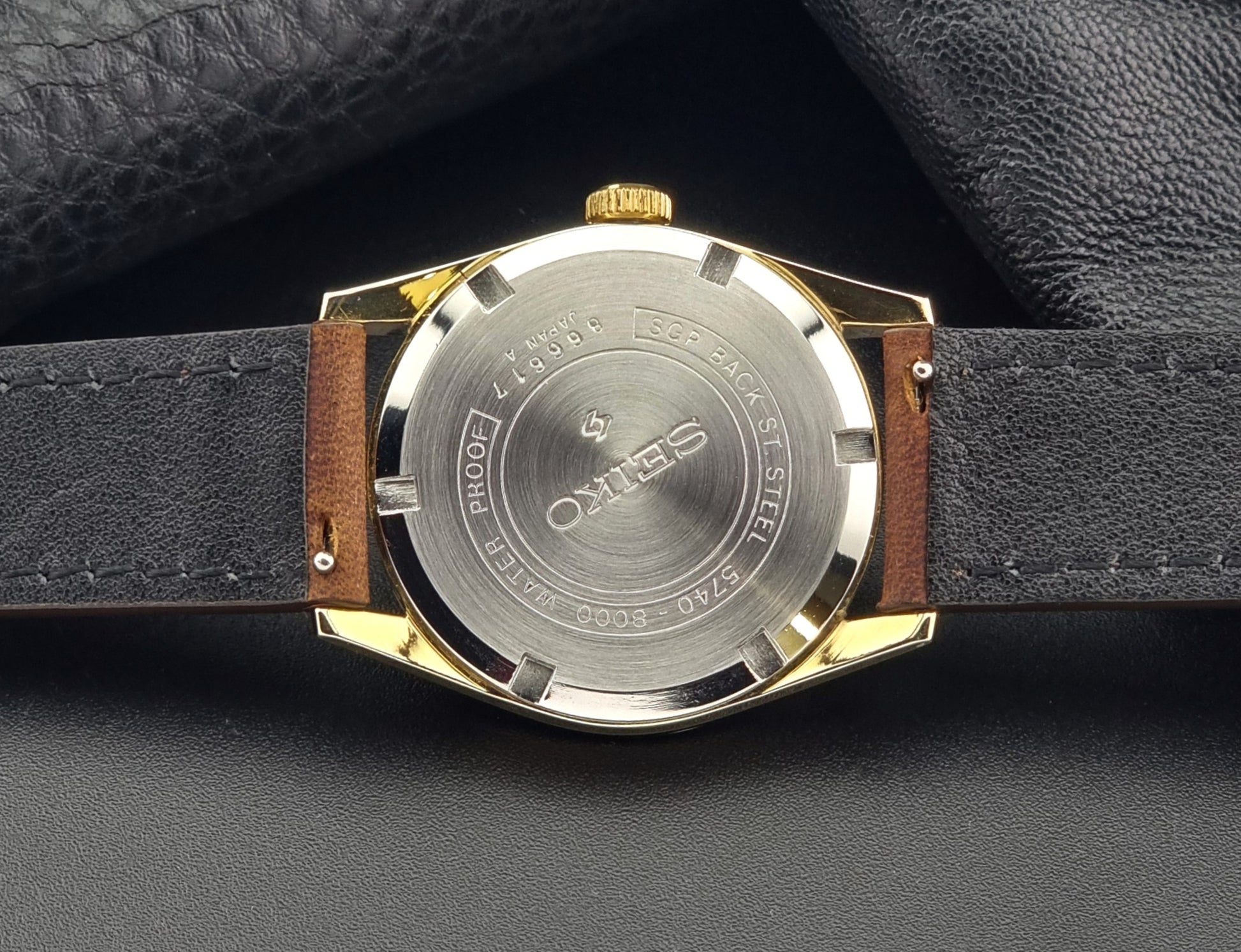 Vintage Seiko Lord Marvel 5740-8000 gold watch with a brown leather strap on a dark gray background case back view